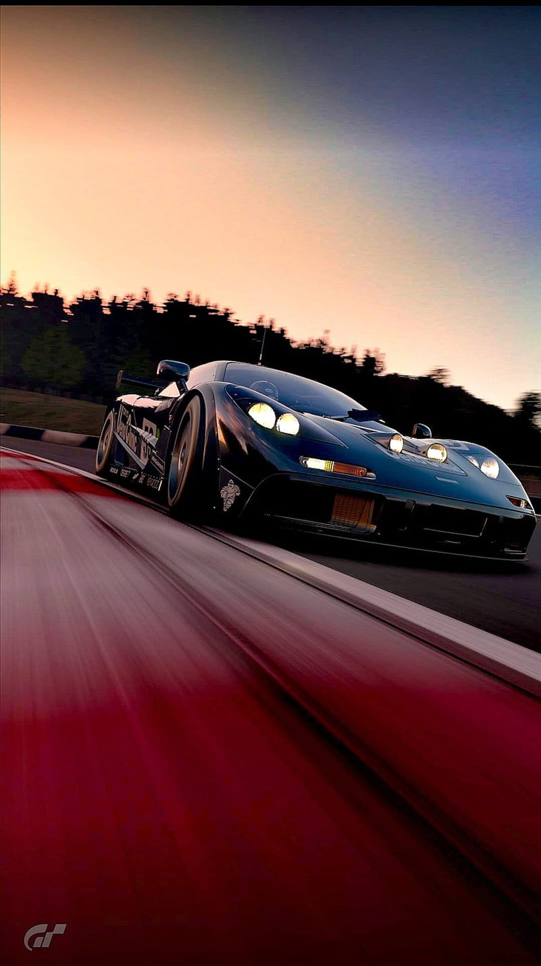 McLaren F1 GTR supercar speeds on a racetrack at sunset with glowing headlights and purple horizon clouds.