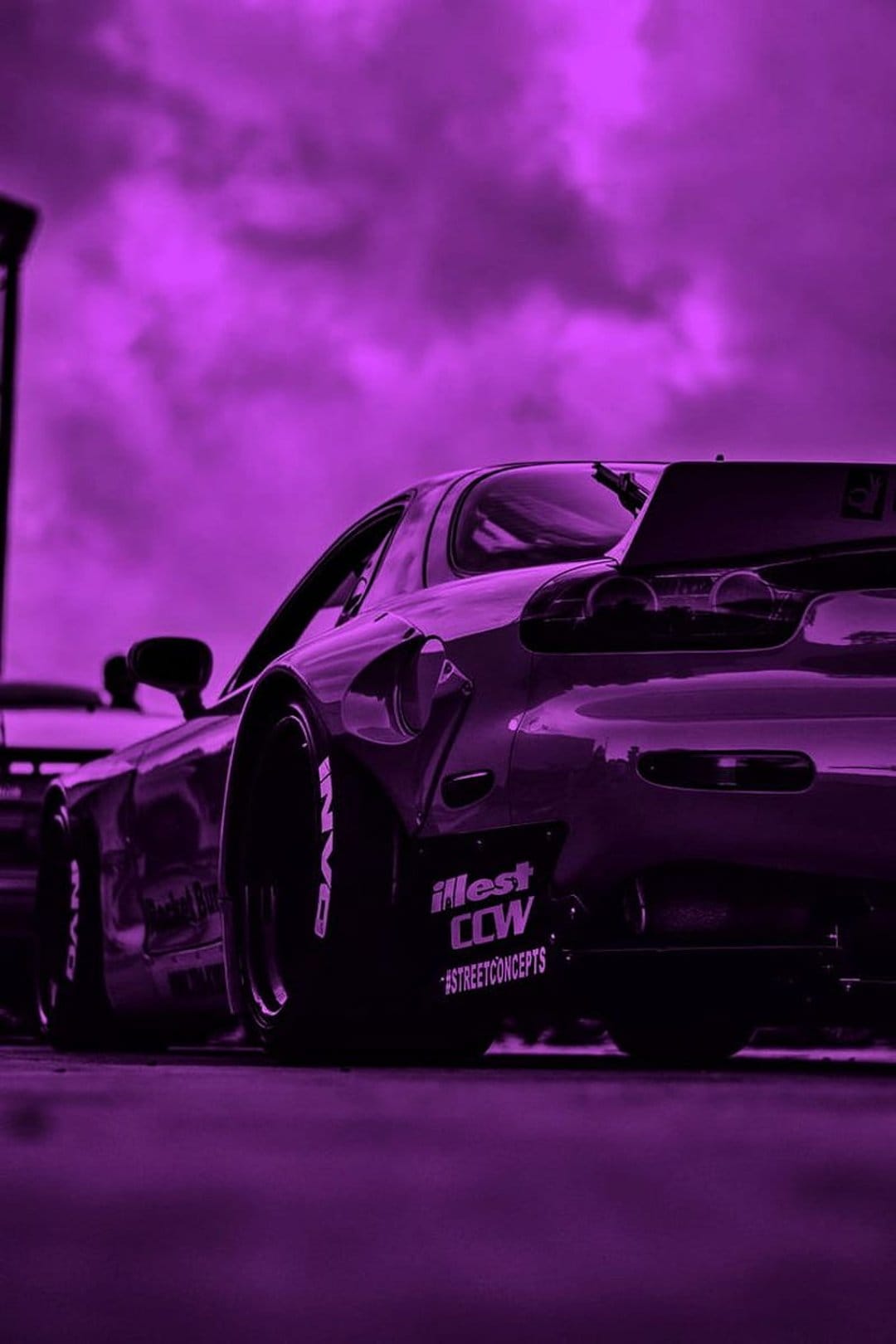 Purple Mazda RX-7 sports car with white stickers and branded tires parked under a moody violet overcast sky.