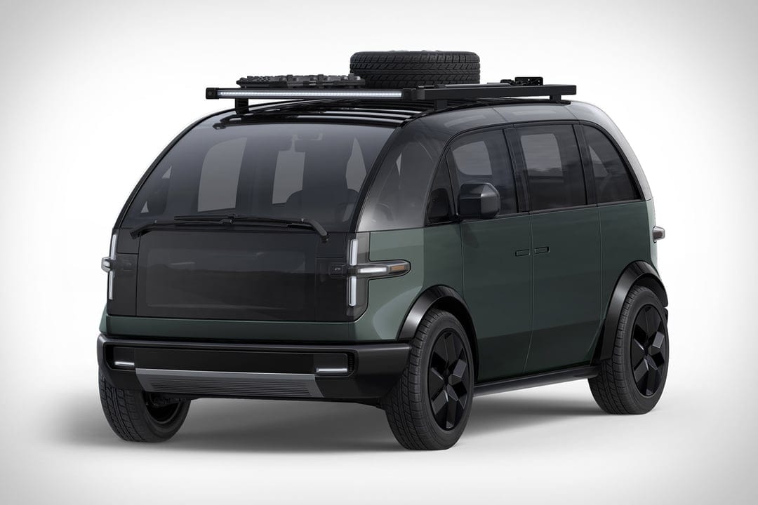 Matte olive green electric adventure van with a roof rack and spare tire on a clean white studio background.