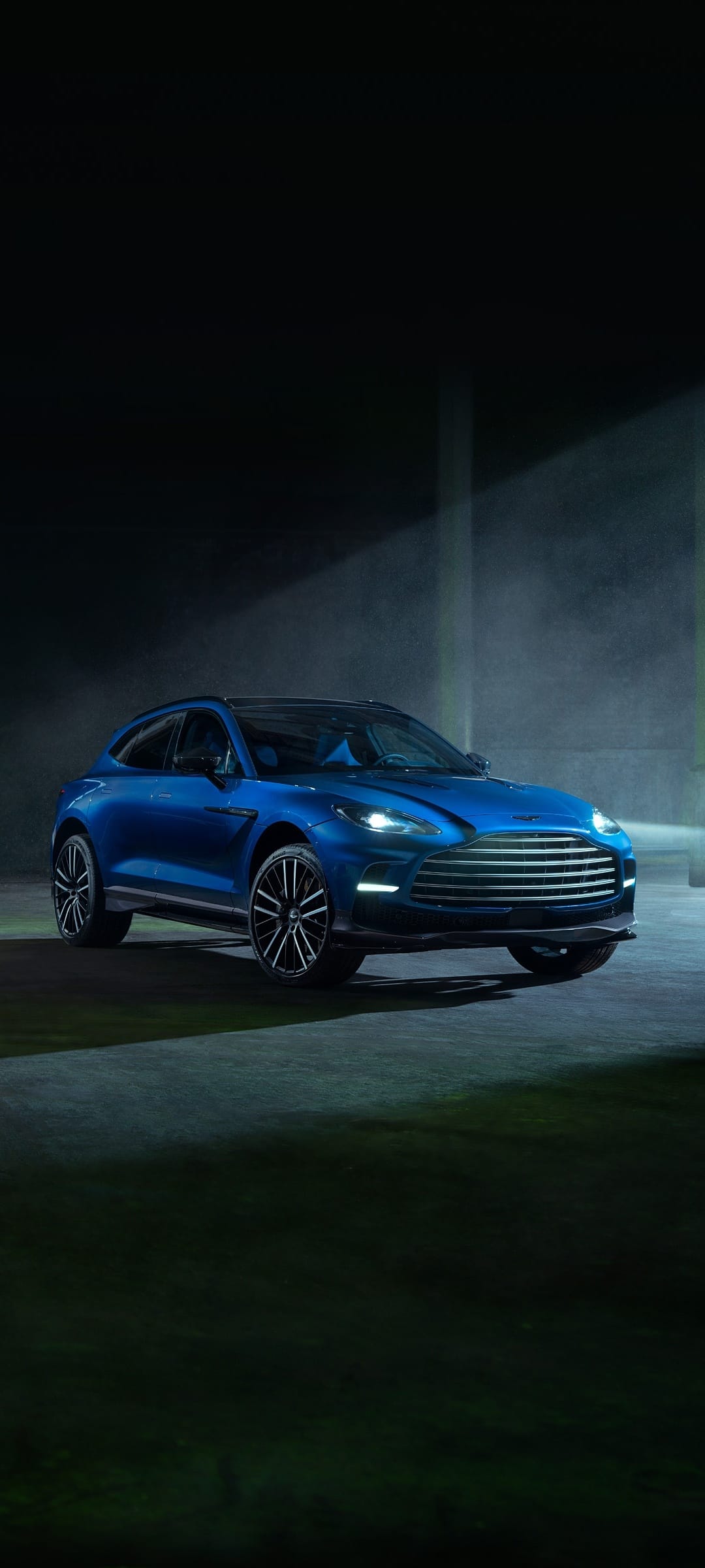 Vibrant blue luxury SUV captured in a dark, moody setting with a cinematic spotlight beam through mist.