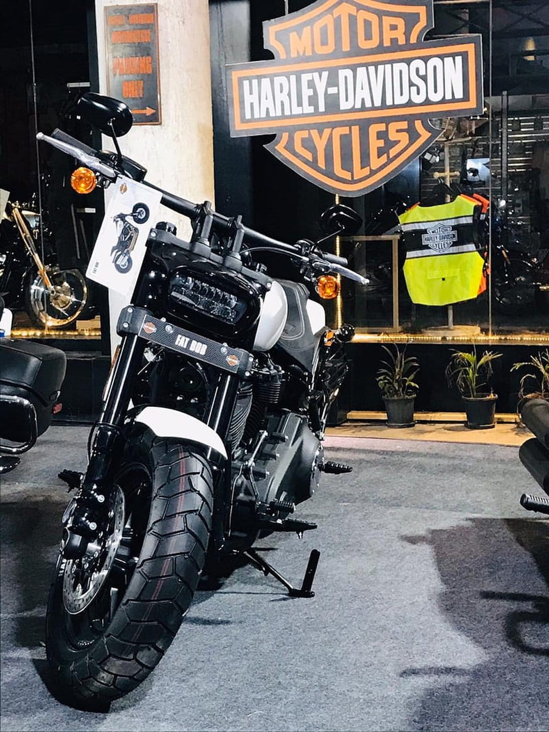 Harley-Davidson Fat Bob motorcycle front end with a bright LED headlight and a yellow safety vest in the background.
