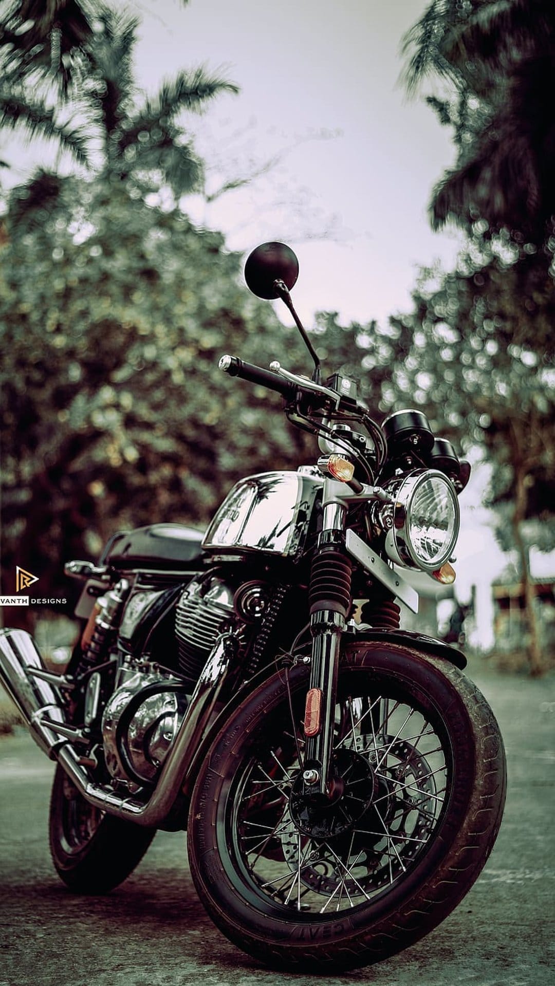 Chrome vintage motorcycle with a round headlight parked on pavement against a blurred green forest background.