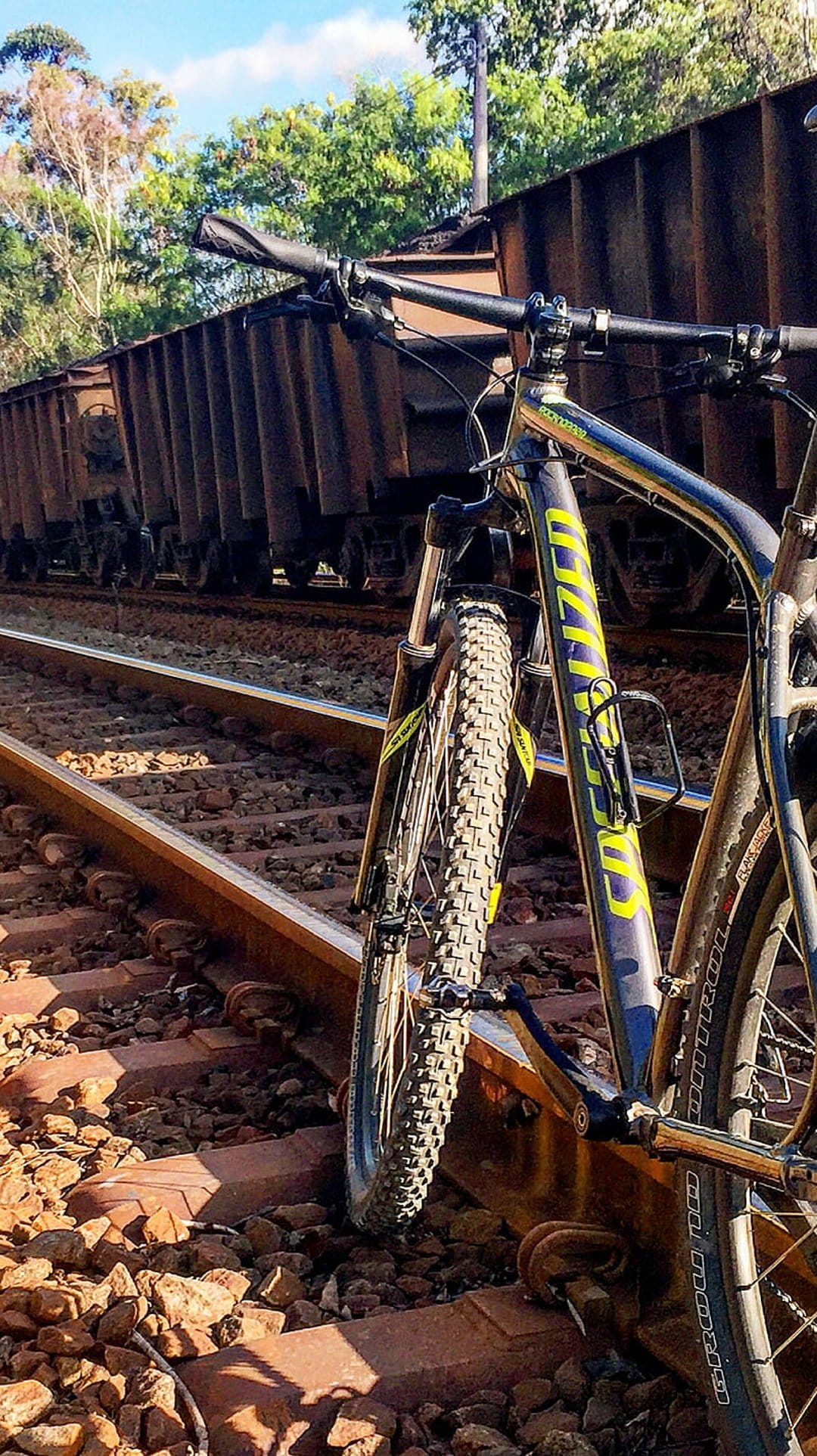 Mountain bike with yellow accents parked on steel railway tracks beside rustic brown metal freight train cars.