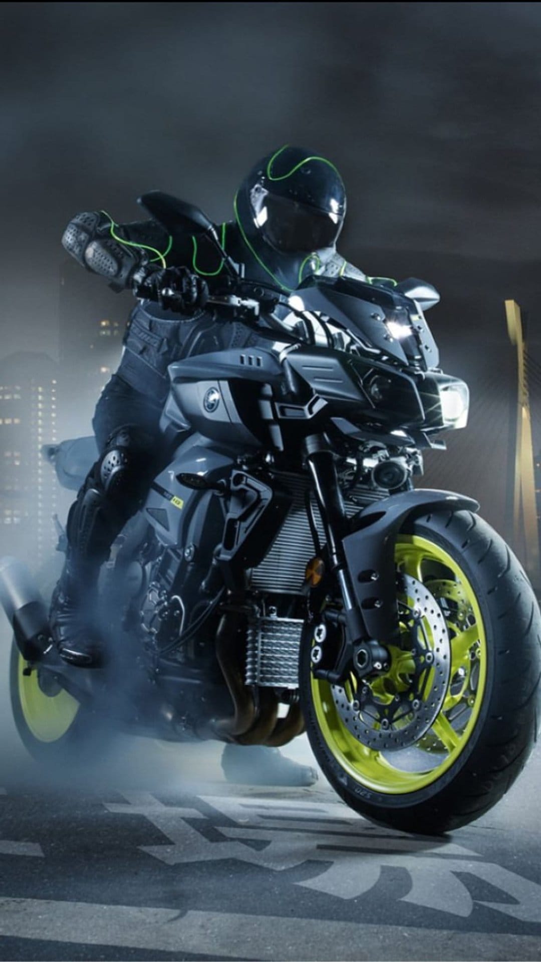 Yamaha MT-10 rider performs a smoky burnout on an urban street at night with glowing yellow wheels.