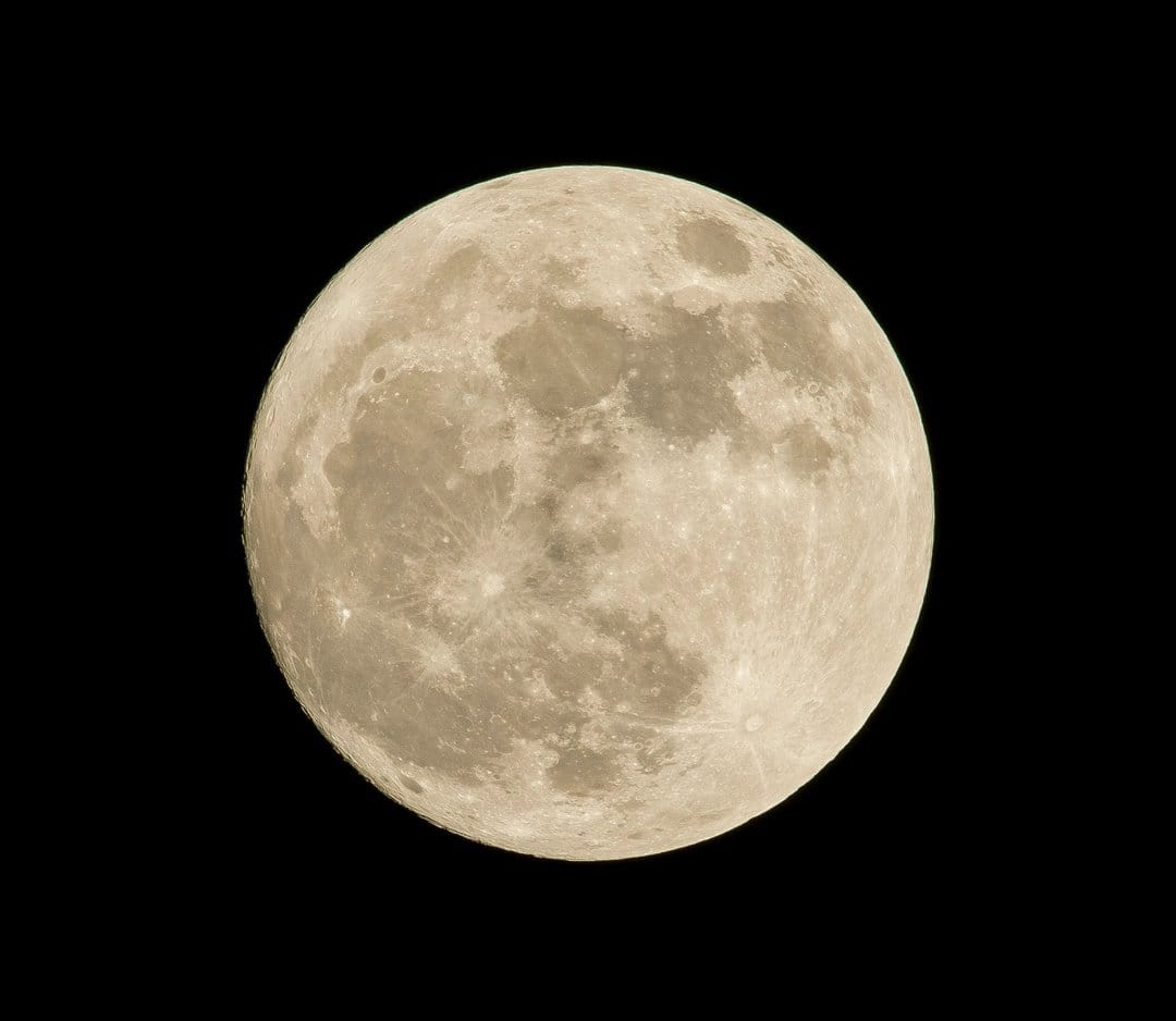 Detailed full moon with gray craters and highland textures centered against a pitch black night sky background.