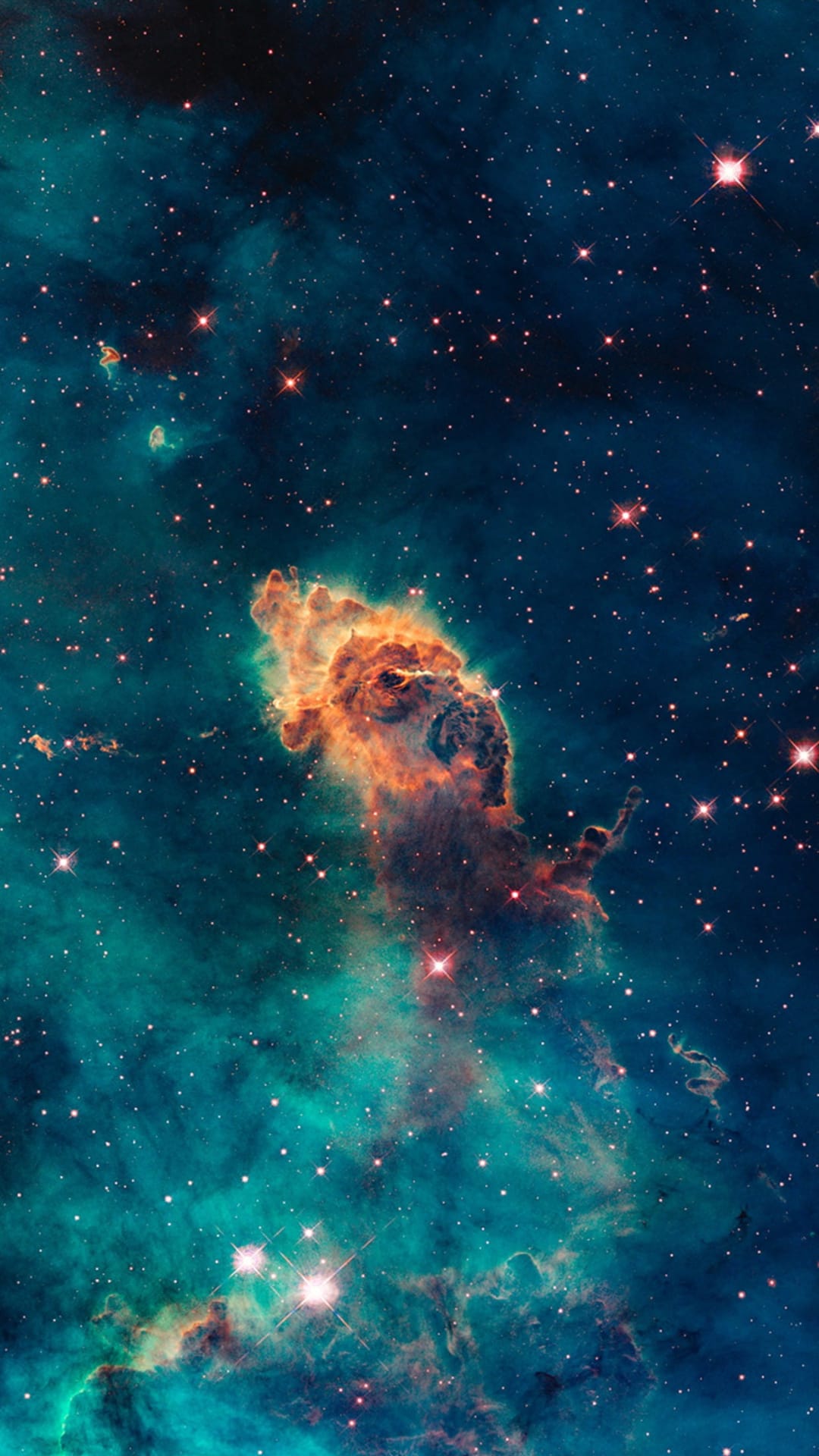 Massive pillars of cosmic gas and dust glow orange against a teal background filled with bright, twinkling stars.