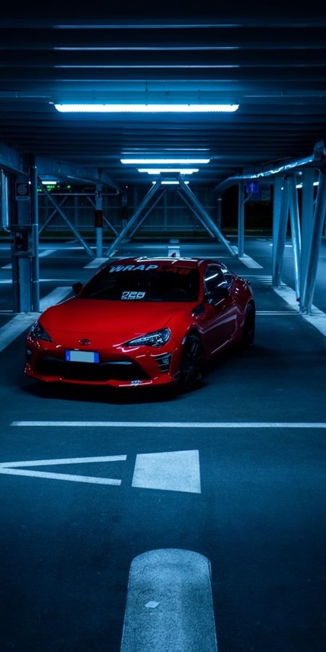 Red sports car parked in a dark garage with blue neon lights reflecting on the polished metal body.