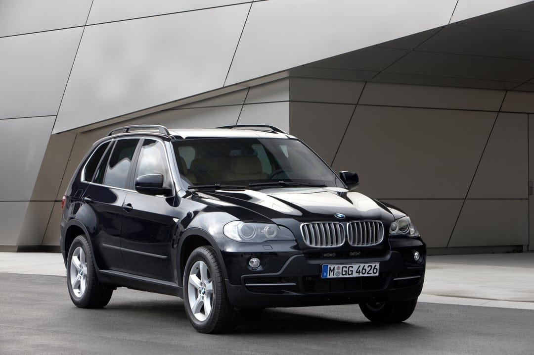 Black BMW X5 parked in front of a modern silver building with sleek architectural lines and soft lighting.