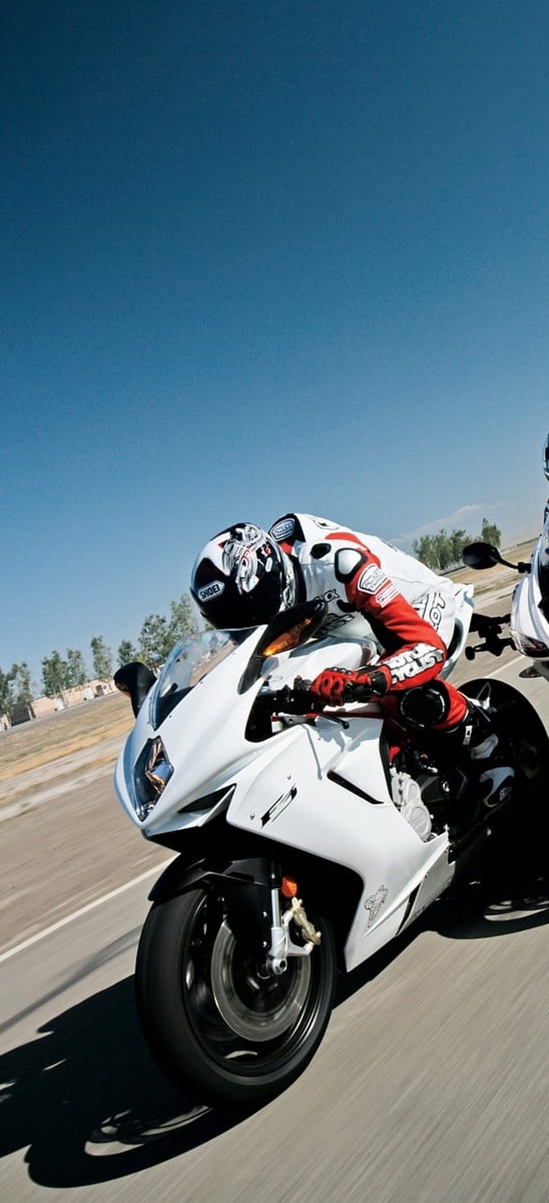 Professional racer on a white sportbike leans into a turn against a clear blue sky during a sunny track day.