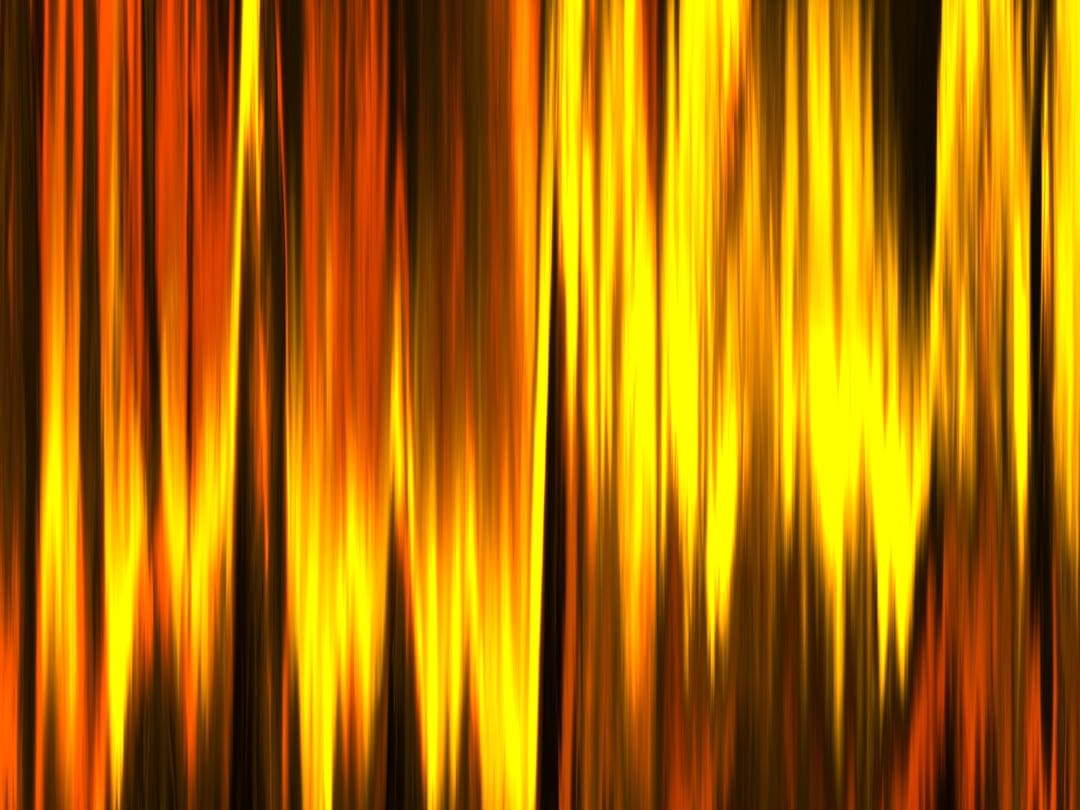 Vertical streaks of vibrant orange and yellow light mimic flickering flames with deep shadows and high contrast.