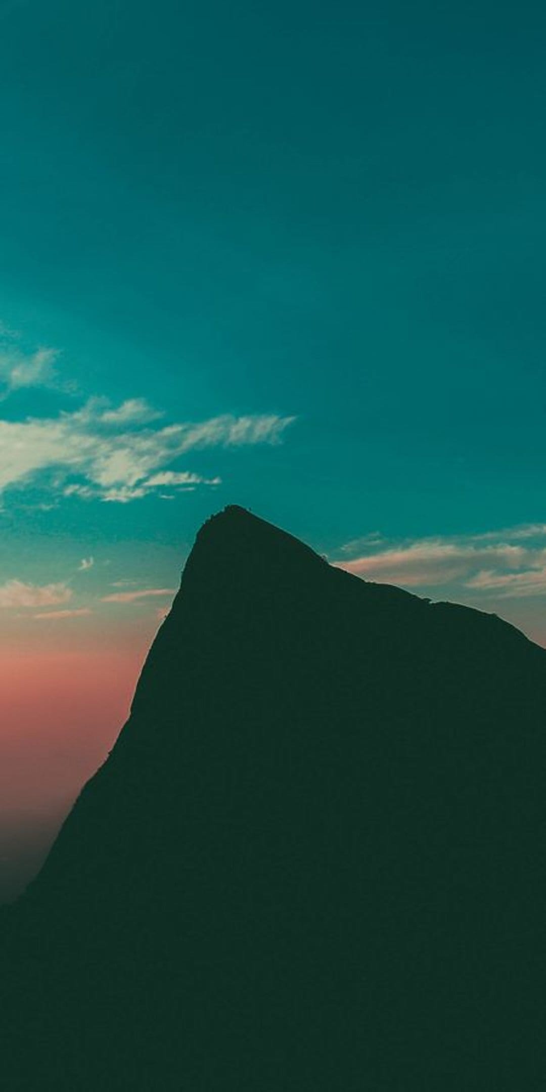 Sharp mountain peak silhouette against a turquoise and orange sunset sky with thin horizontal clouds.