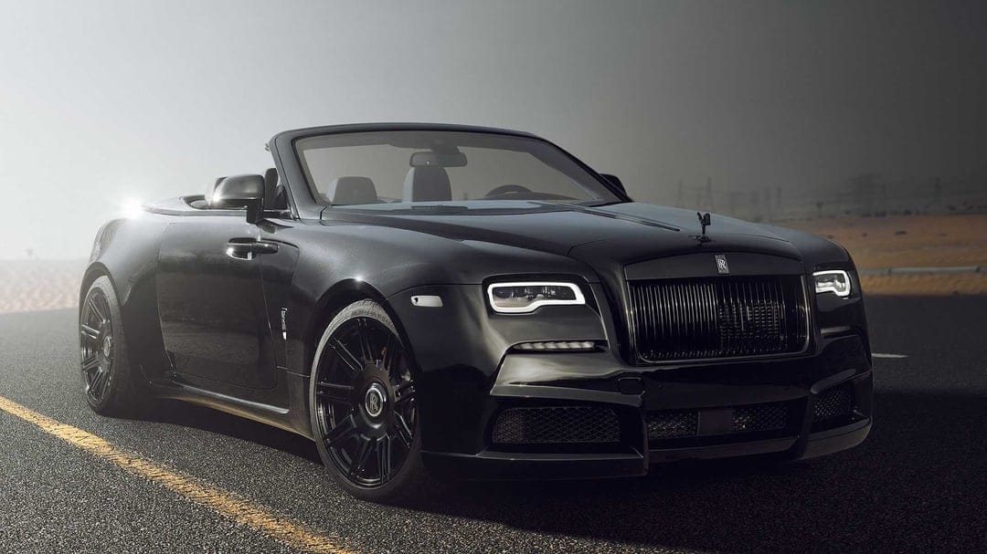 Black Rolls-Royce convertible with widebody kit on a desert road during a moody sunset landscape scene.