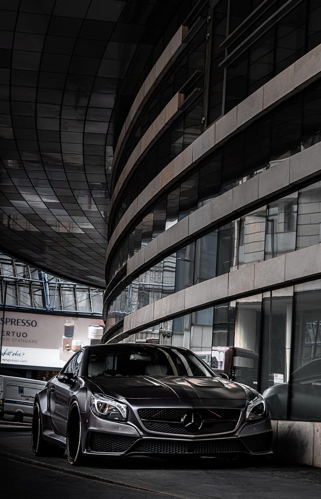 Mercedes-Benz CLA coupe parked in front of a curved glass building with dark metallic reflections at night.
