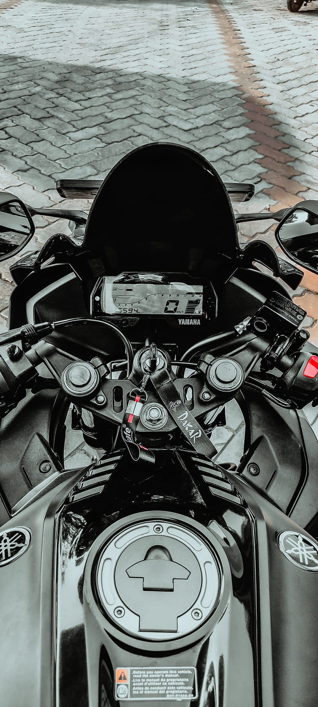 Yamaha R15 digital dashboard and fuel tank cap viewed from above, highlighting handlebars and a dakar keychain.