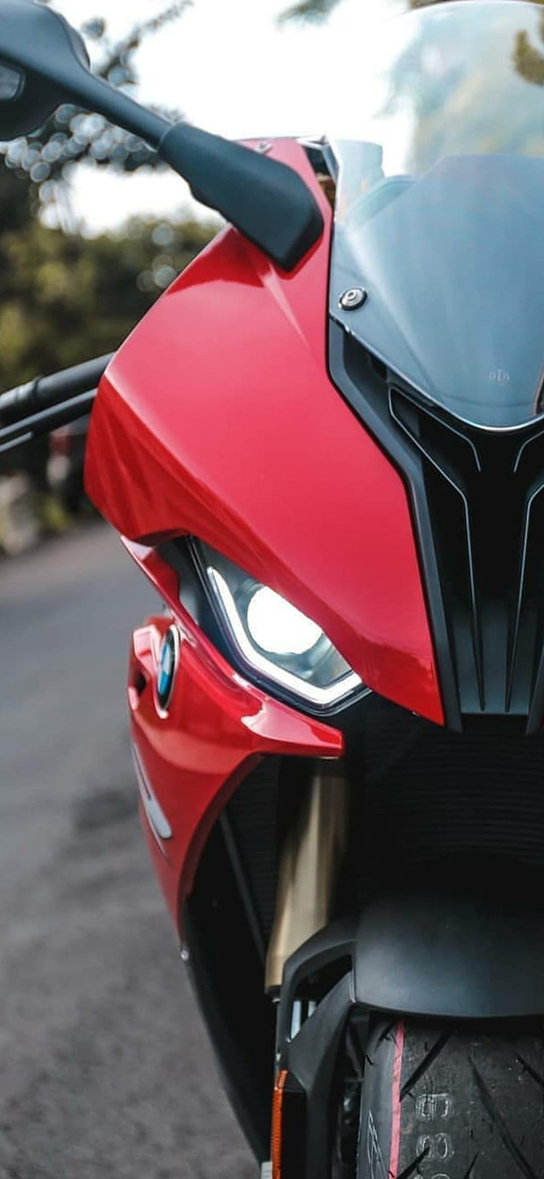 Red BMW S1000RR front fairing and LED headlights with a black grille and tire tread in a vertical close-up.