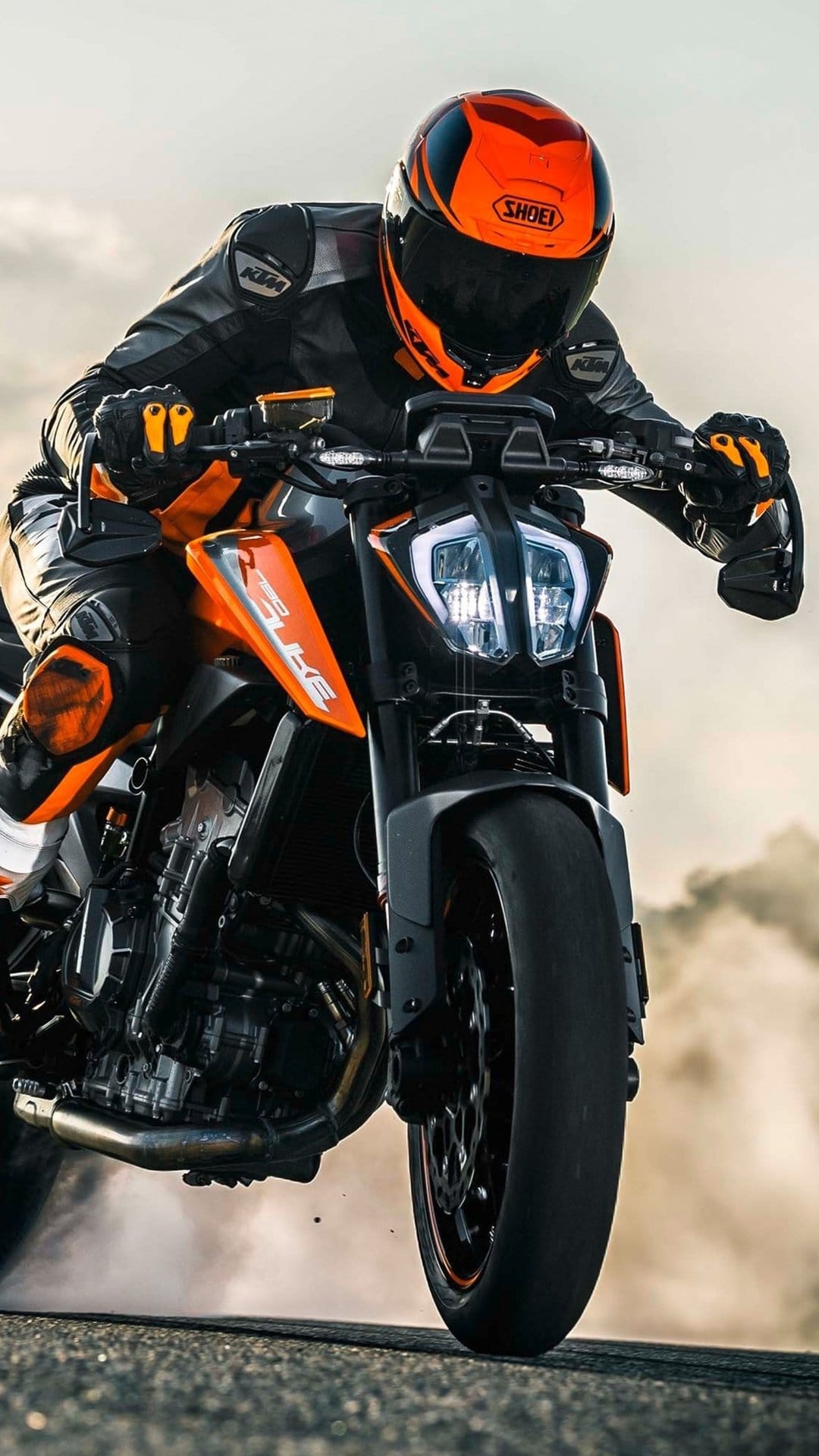 KTM motorcyclist in orange racing gear leans into a sharp turn with thick smoke billowing from the rear tire.