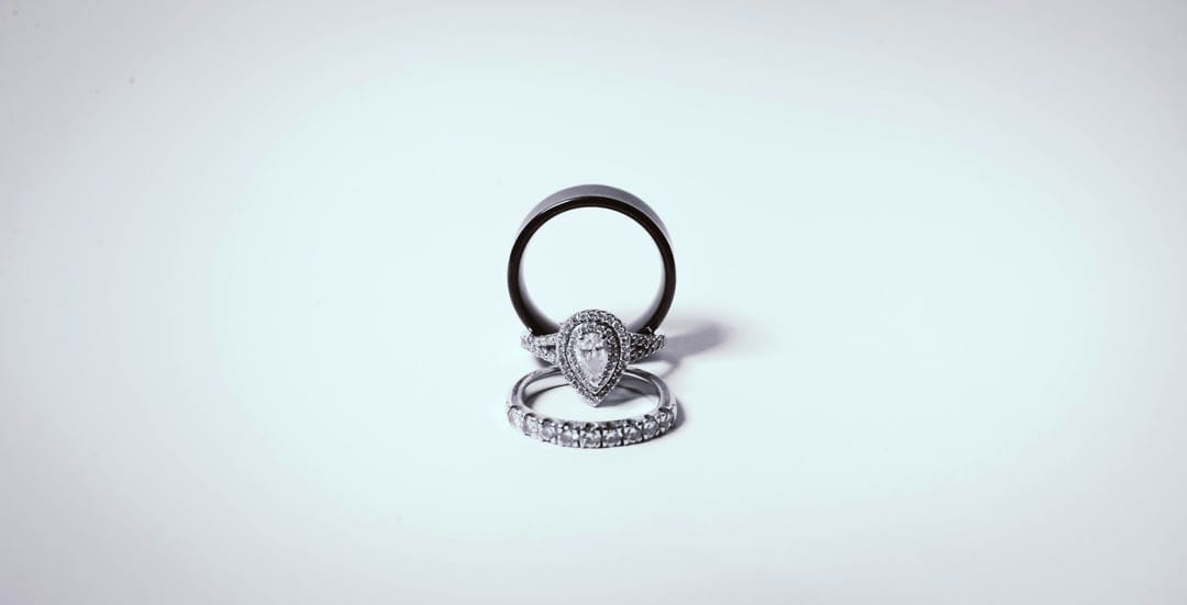 Pear-shaped diamond engagement ring and two wedding bands stacked together on a minimalist white background.