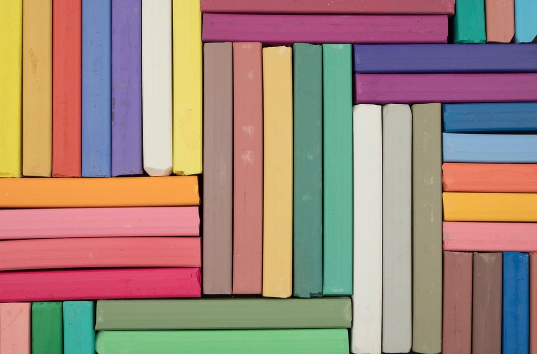 Pastel chalk sticks arranged in color-coded rows from a top-down view with soft matte textures and pigment dust.
