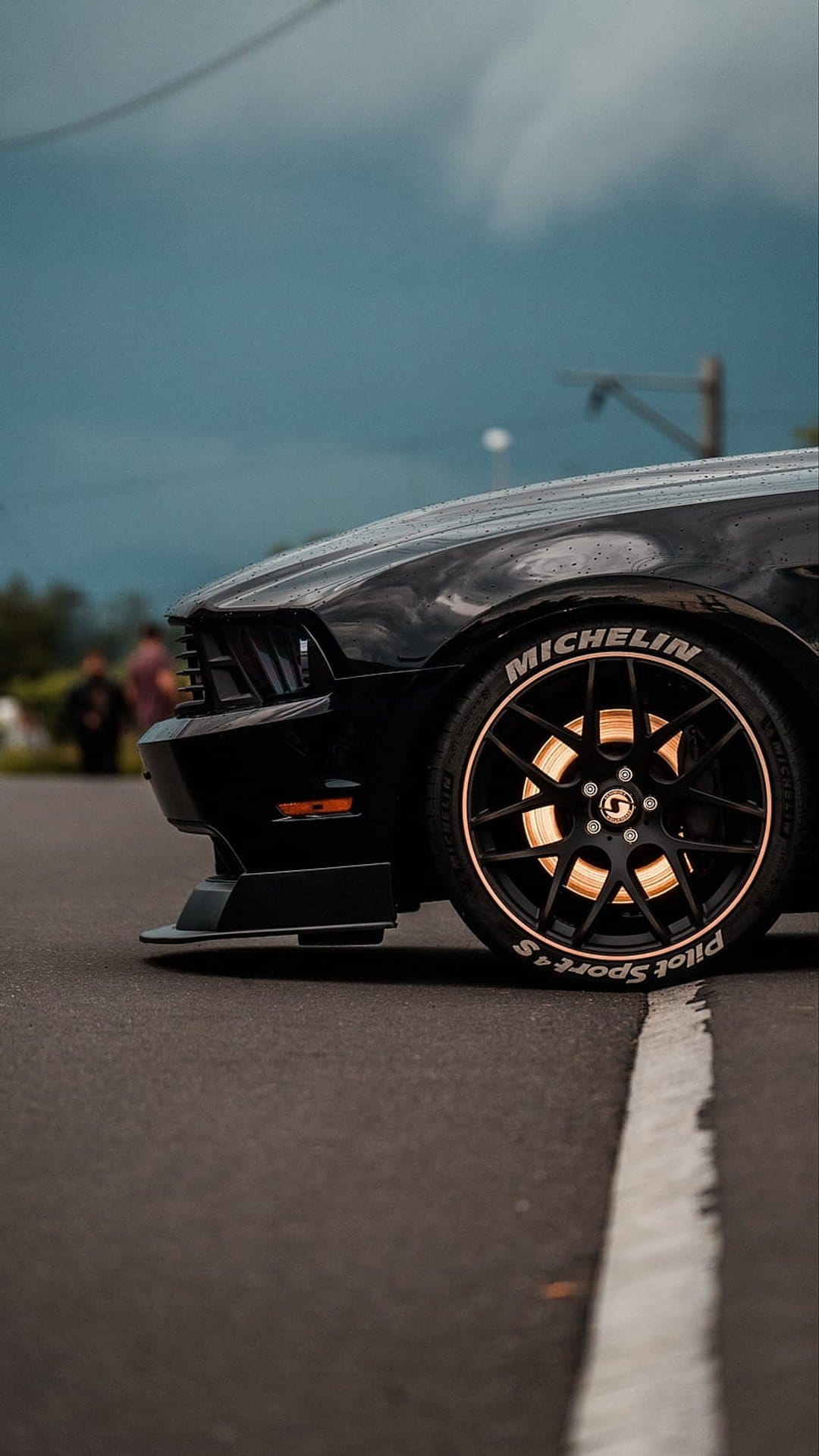 Black Ford Mustang wheel and front fender with Michelin Pilot Sport 4S white tire lettering under a moody sky.
