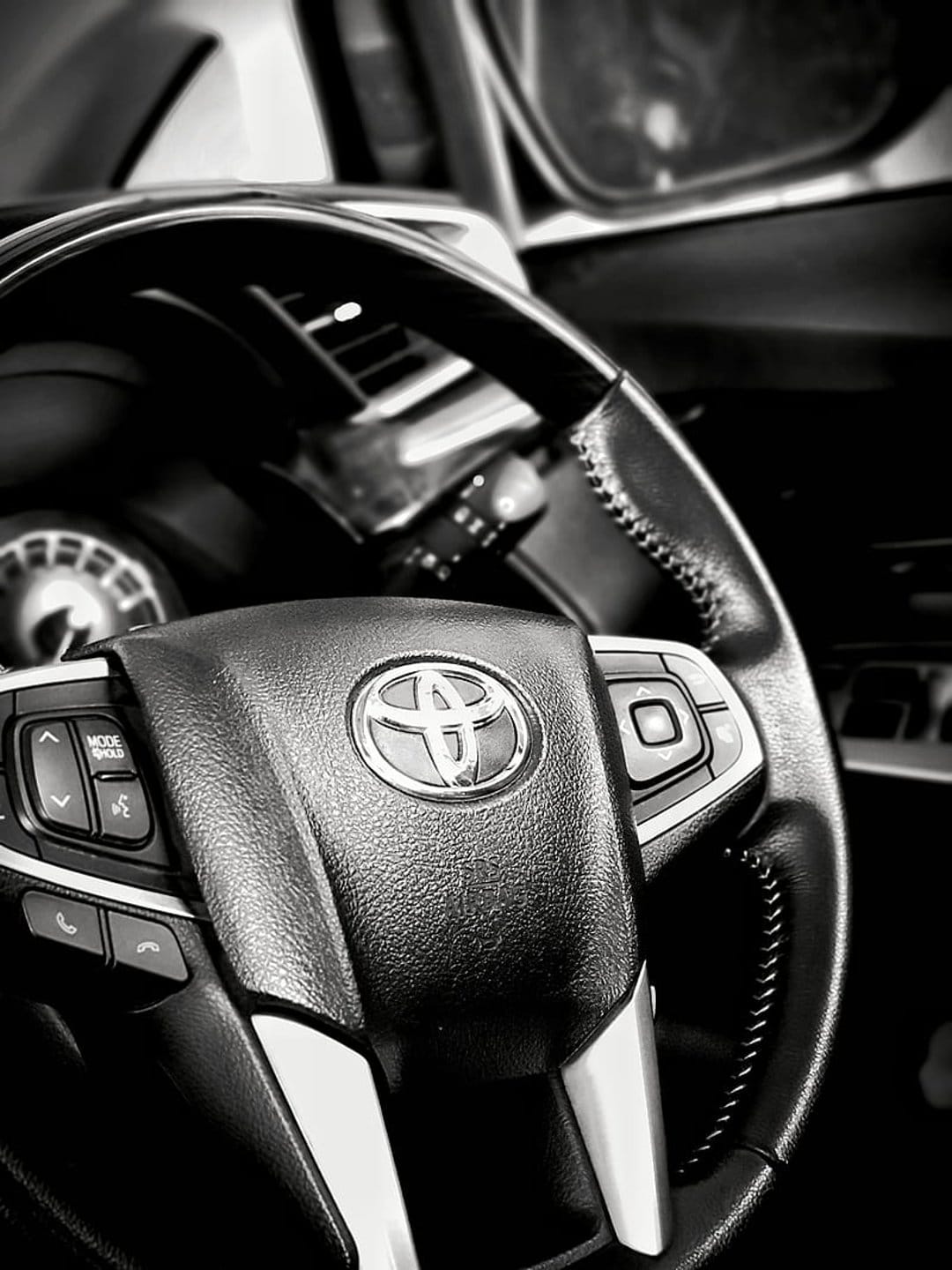 Toyota steering wheel emblem and integrated control buttons featured in a high-contrast black and white macro shot.