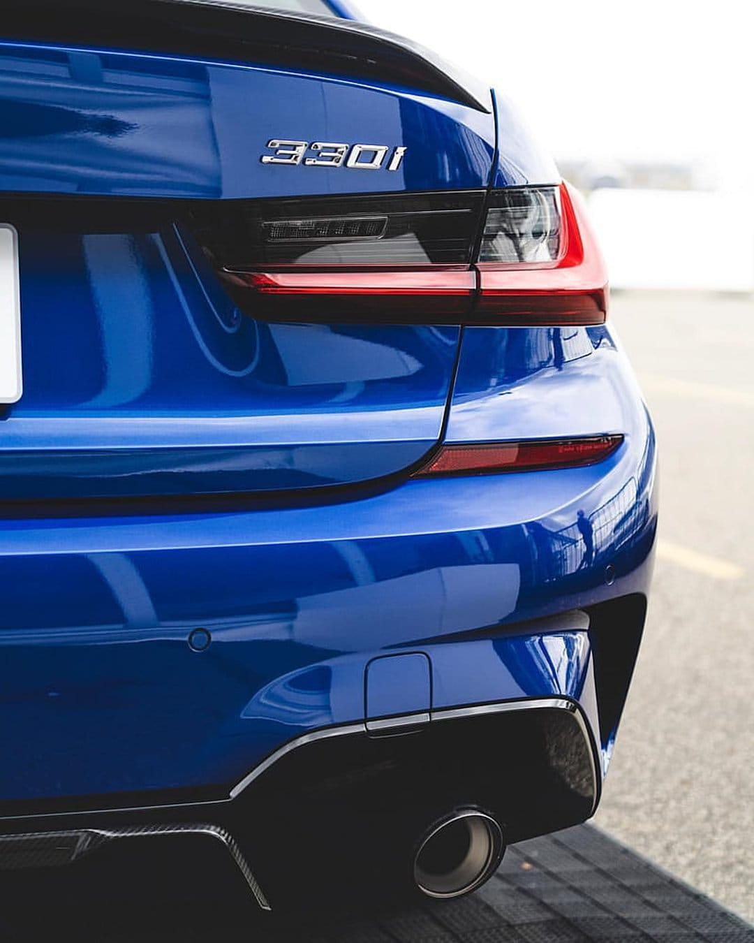 BMW 330i blue rear bumper and red LED taillight with carbon fiber accents and polished chrome exhaust tips.