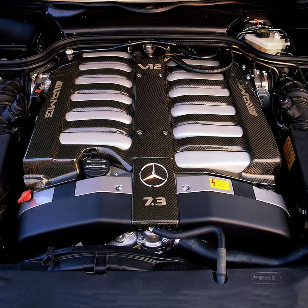 AMG V12 7.3 engine bay displays woven carbon fiber manifolds and silver runners in a high-performance setup.