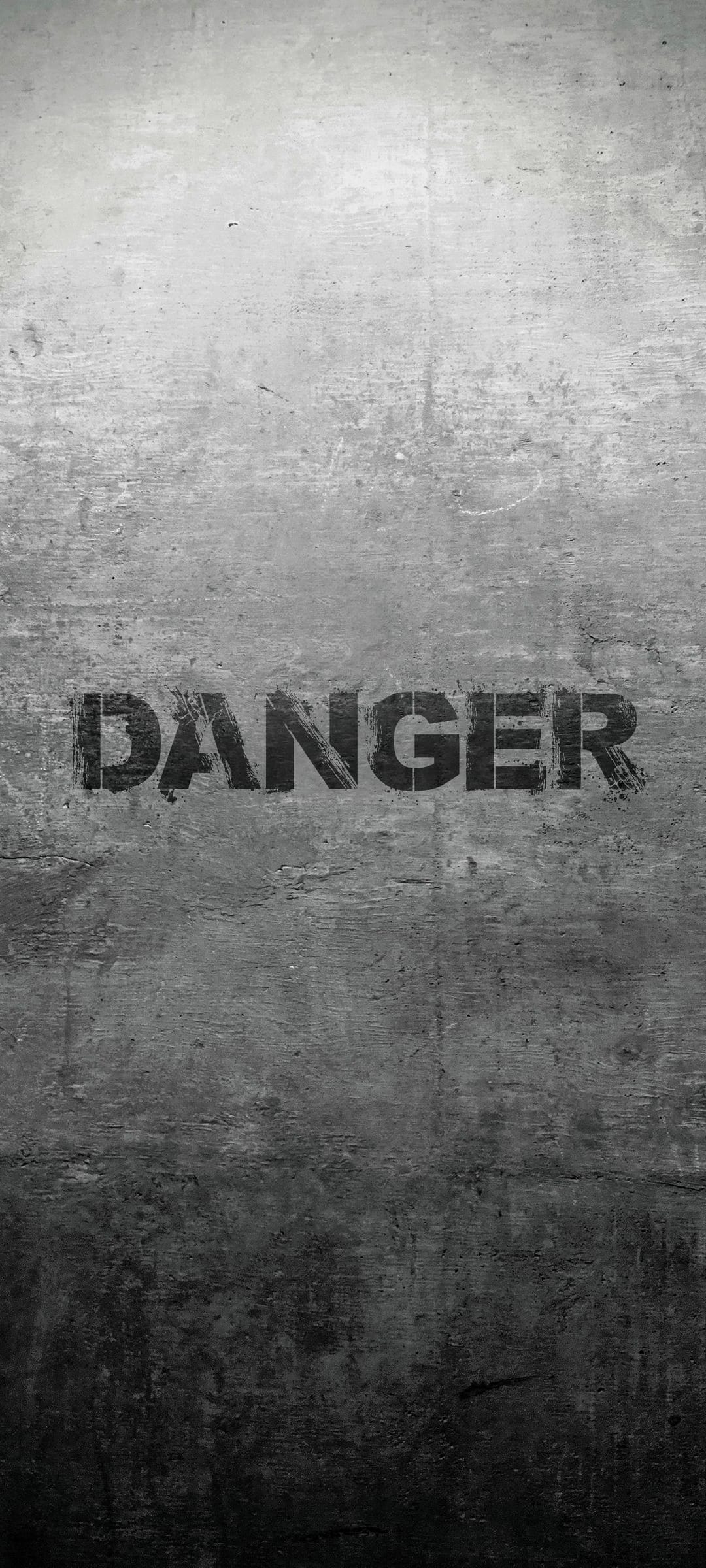 Danger sign stenciled on a scratched grey concrete wall with visible cracks and heavy industrial texture.