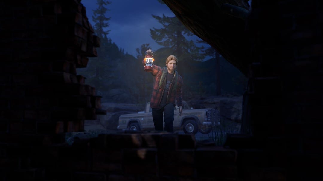Man in red flannel holding a glowing lantern at night by a truck, framed through a broken brick wall.