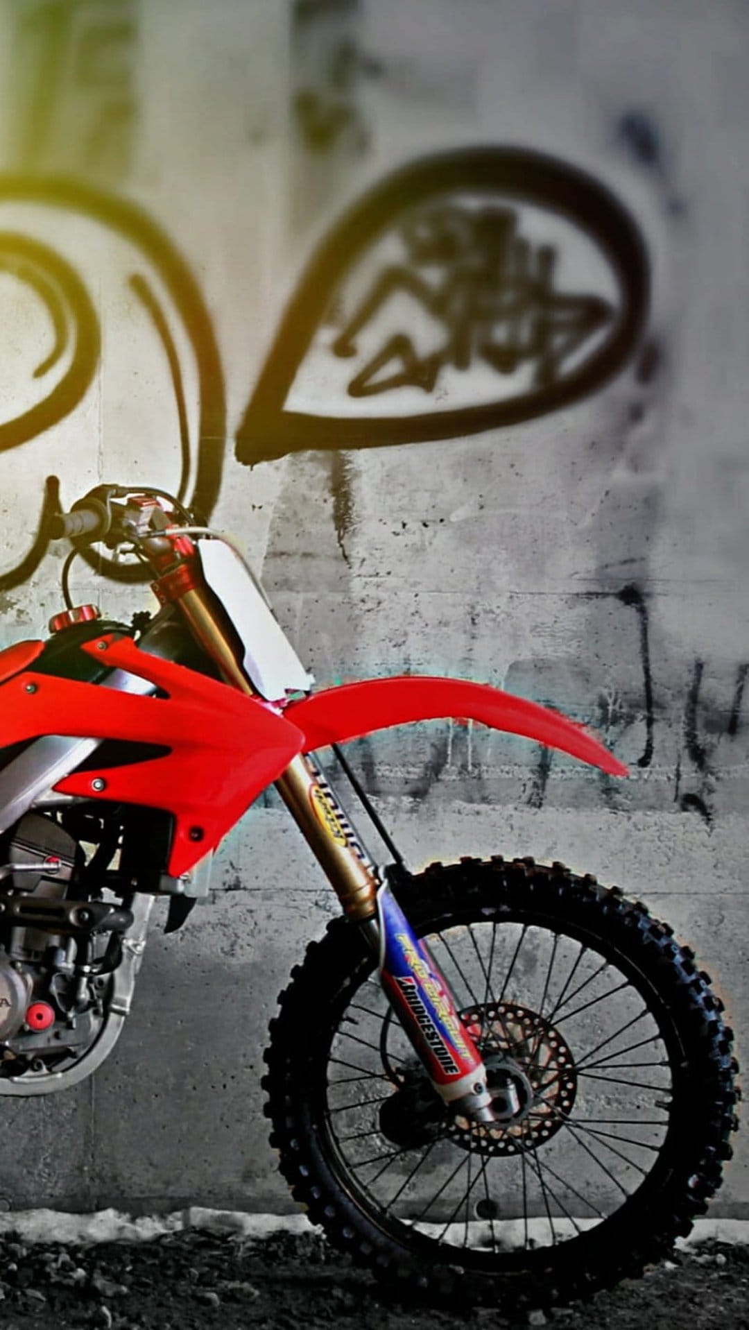 Red motocross bike front wheel and suspension parked in front of a colorful graffiti wall with urban street art.