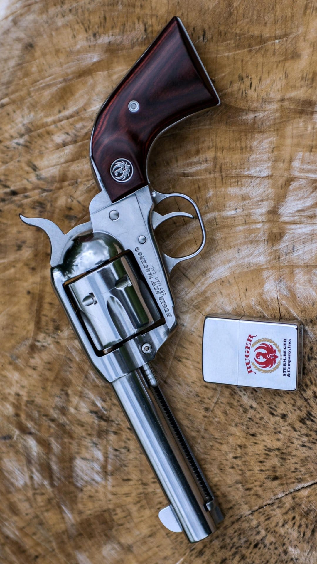 Ruger New Vaquero revolver and a white Zippo lighter lay on a weathered wooden surface in a top-down view.