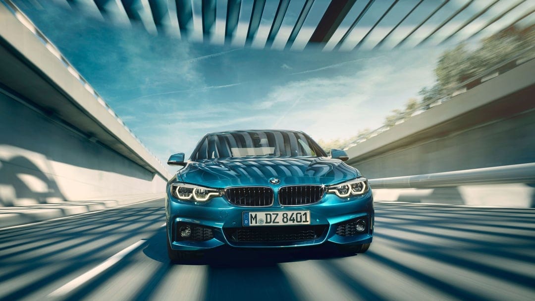 Blue BMW sports sedan driving through a modern tunnel with motion blur and overhead architectural lighting.