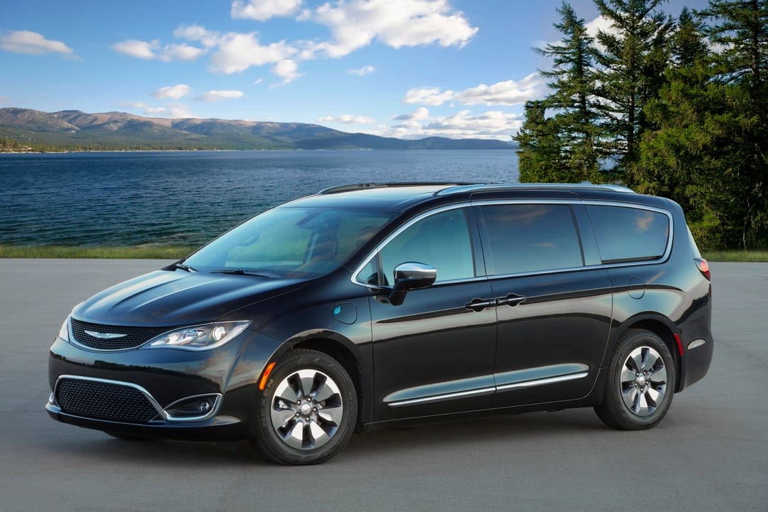 Black Chrysler Pacifica Hybrid parked on a road beside a blue lake with distant mountains and a clear sky.