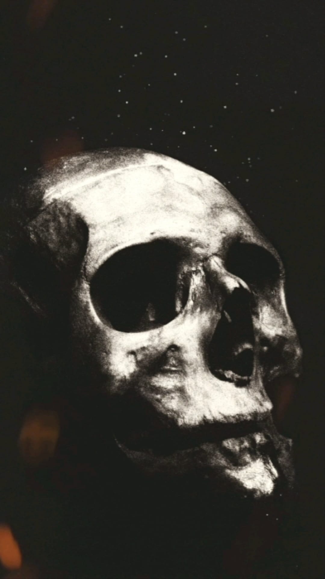 Human skull with deep eye sockets against a starry sky with orange fire light reflecting on the jaw and teeth.