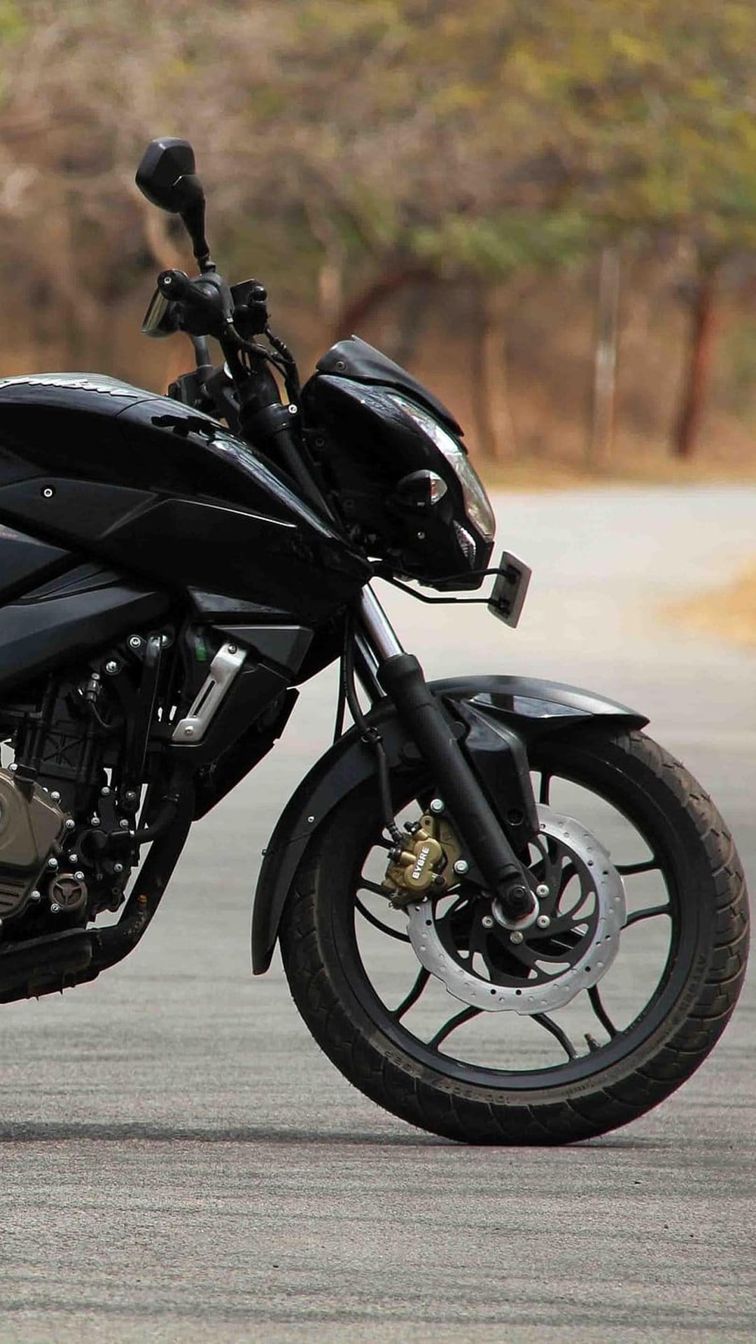 Black sport motorcycle with visible front disc brakes and suspension parked on an asphalt road with blurred trees.