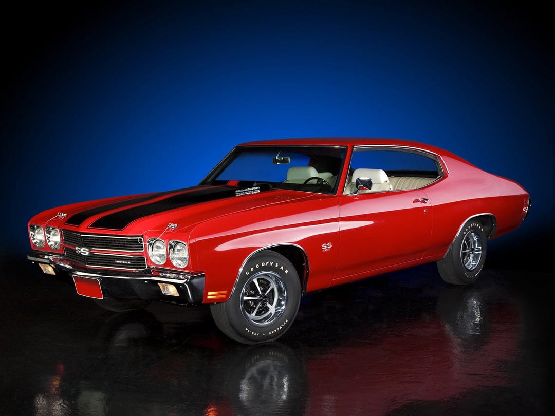 Red 1970 Chevrolet Chevelle SS with black hood stripes and white interior on a reflective studio floor.