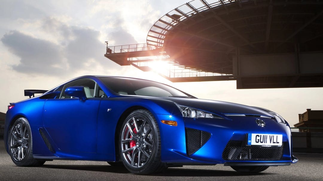 Blue Lexus LFA supercar parked under a circular structure with bright sun flare and red brake calipers.