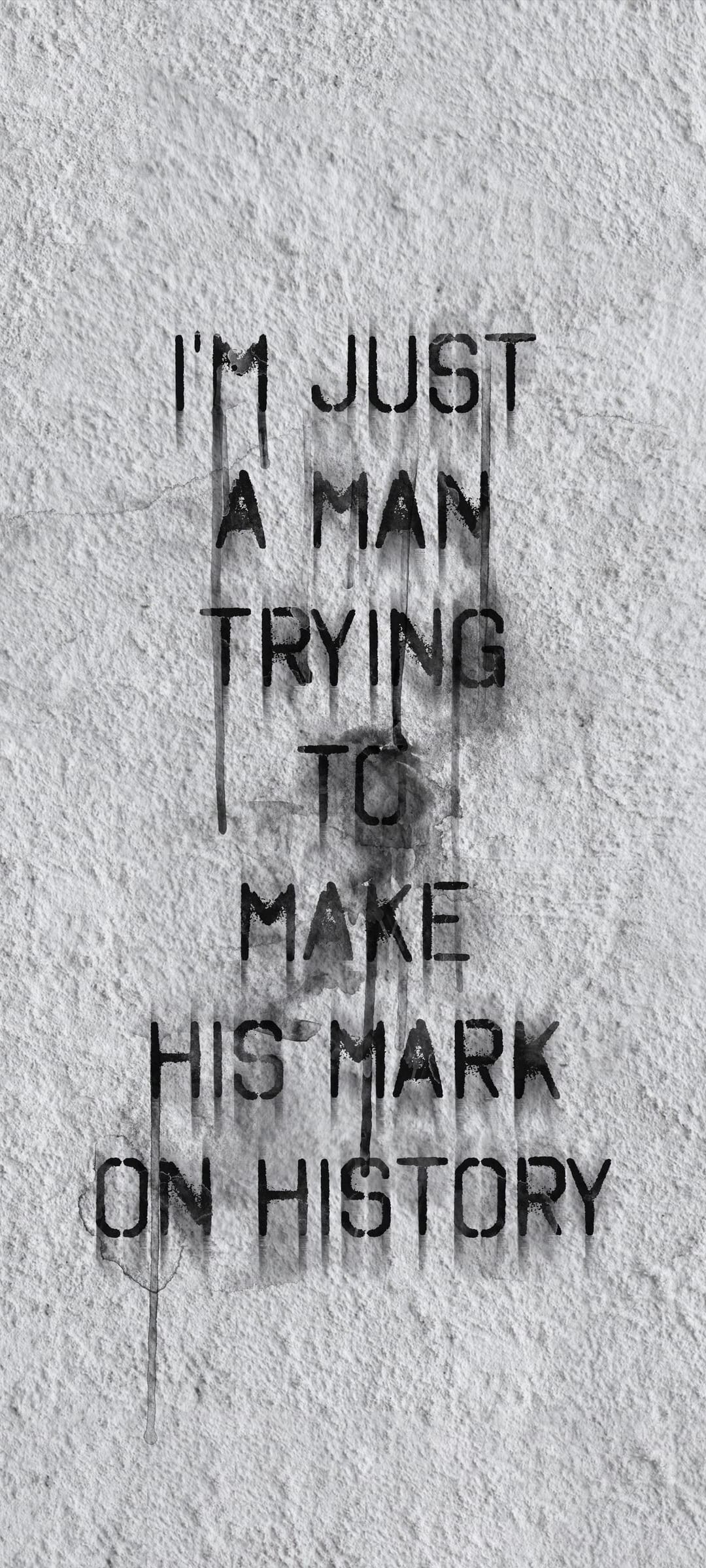 Black stencil text with dripping paint on a white textured wall states I'm just a man trying to make his mark.