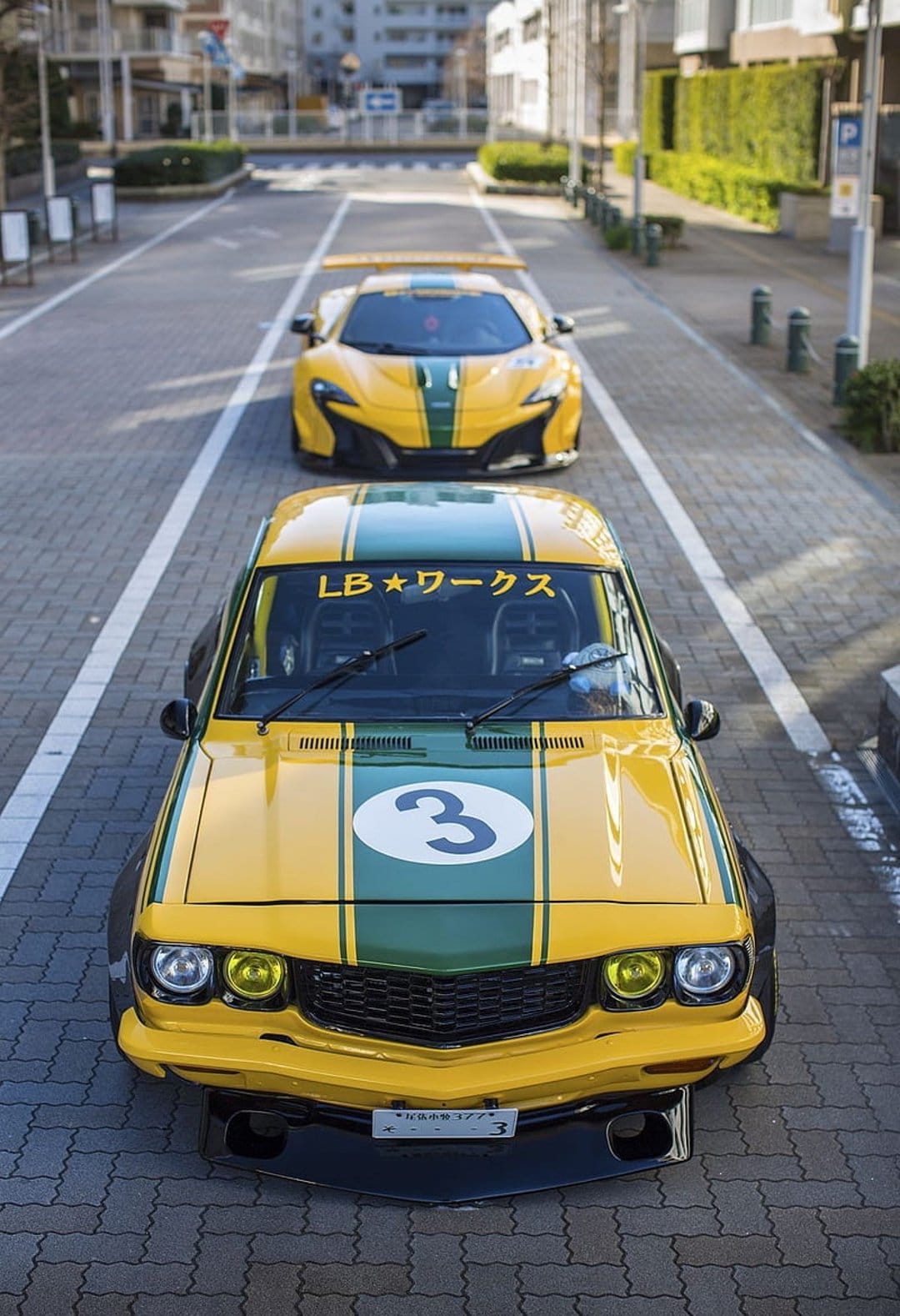 Modified vintage racing car with a yellow and green livery and LB Works decals parked on an urban street.