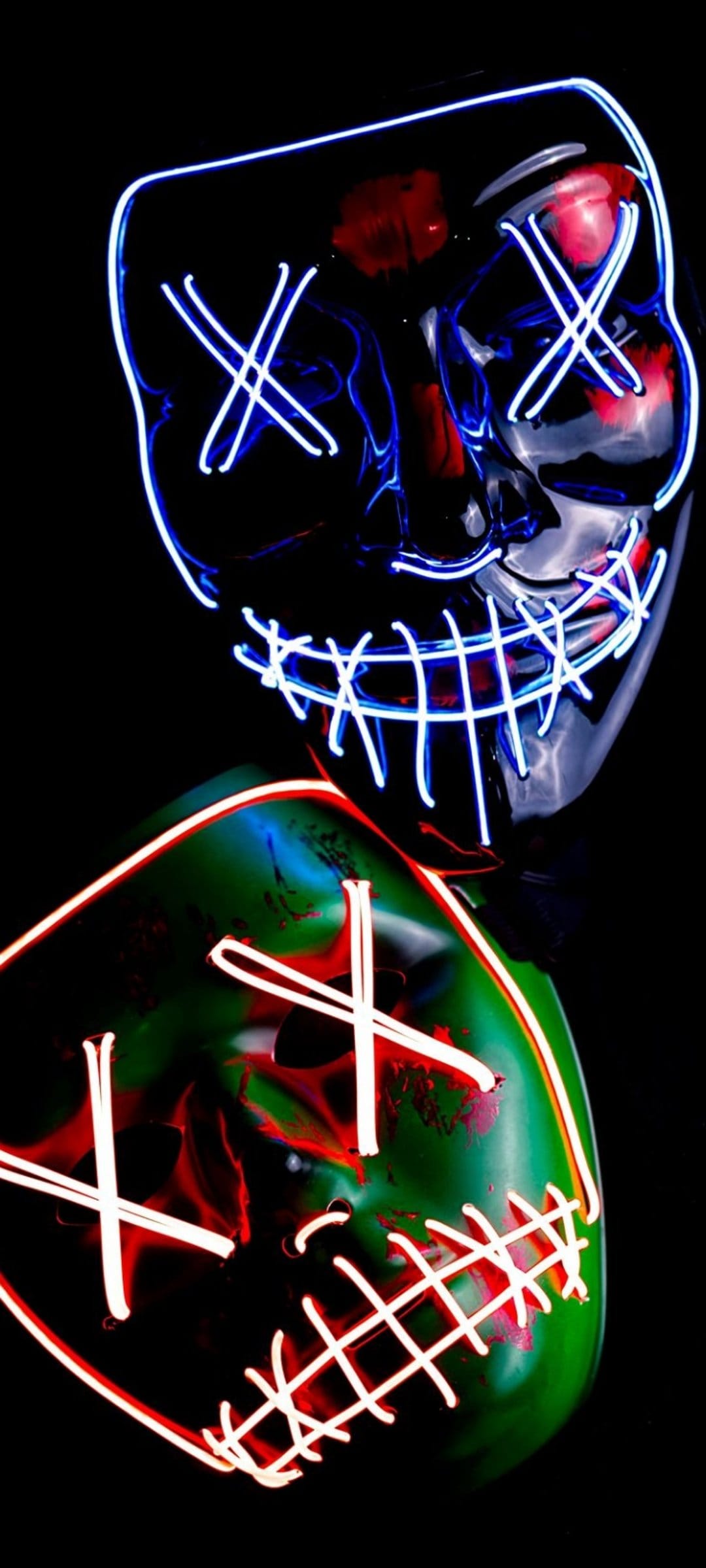 Two glowing LED masks with X-shaped eyes and stitched mouths emit blue, green, and red light on a black backdrop.