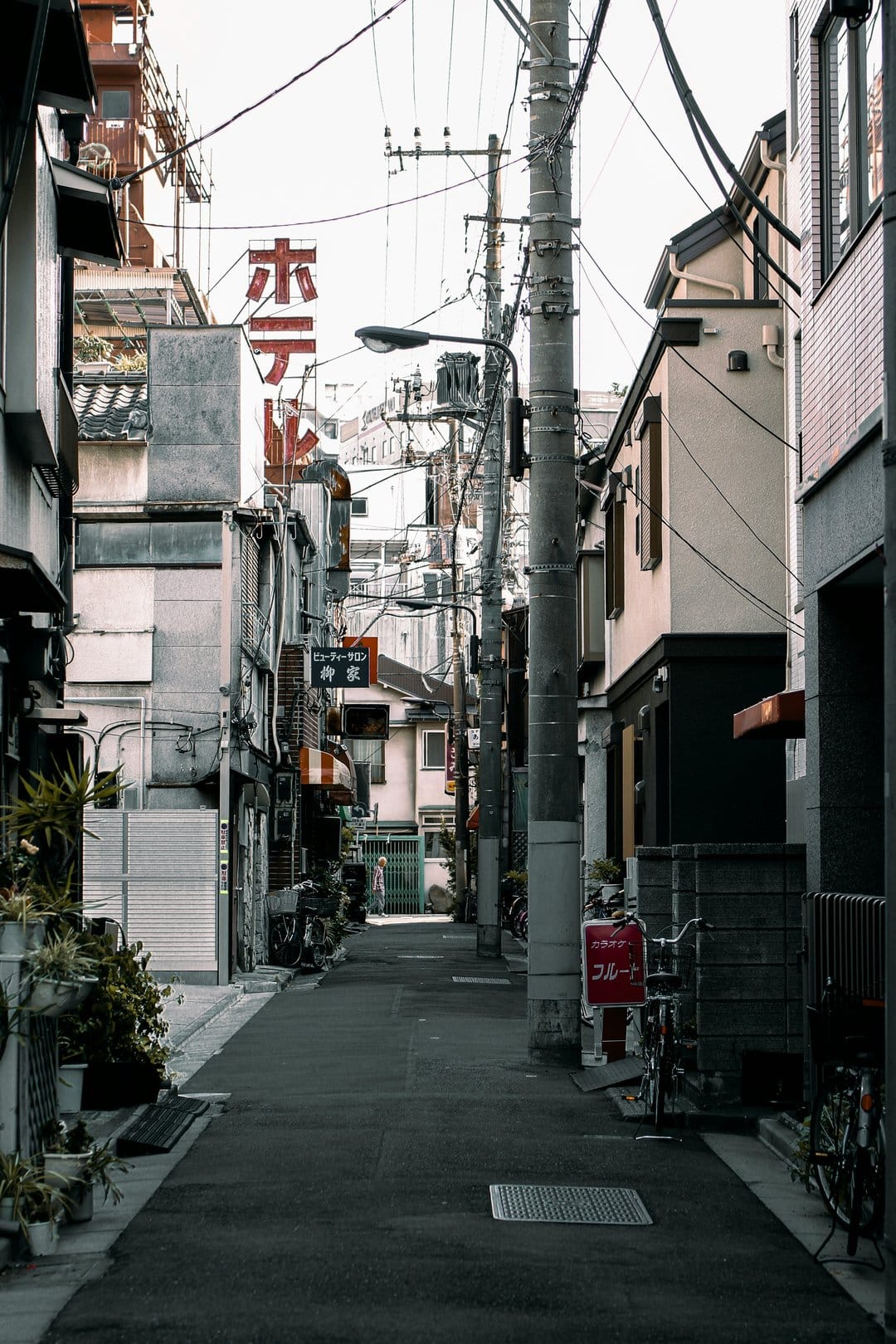 Narrow Japanese alleyway featuring traditional buildings, overhead utility wires, and red vertical street signs.