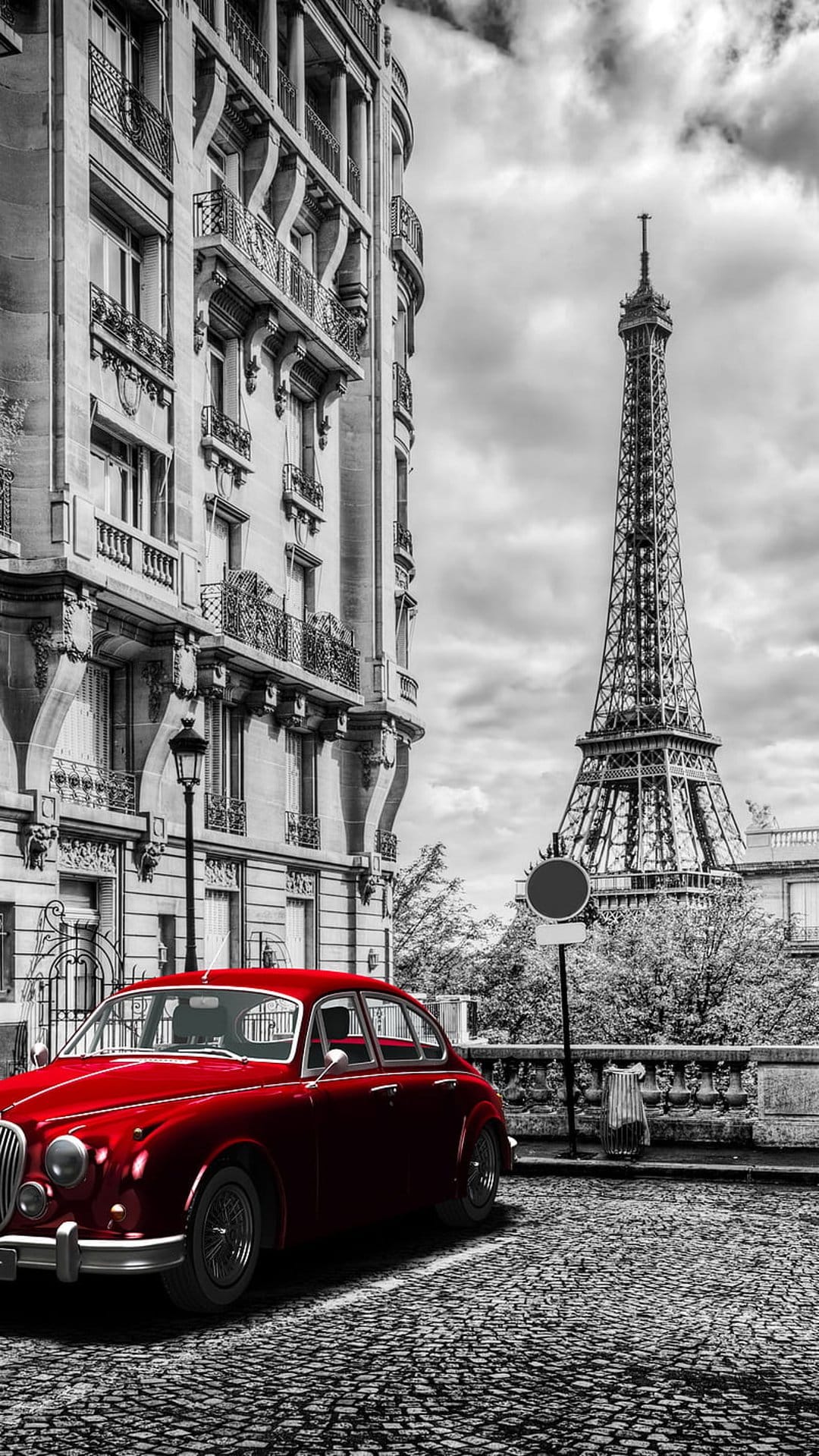 Vintage red car parked on a cobblestone Paris street with the Eiffel Tower standing in the background.