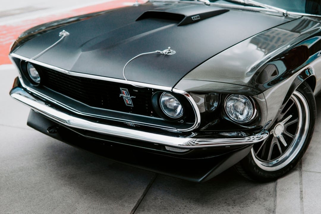 Classic black Ford Mustang front end showing a chrome pony emblem, mesh grille, dual headlights, and hood scoop.