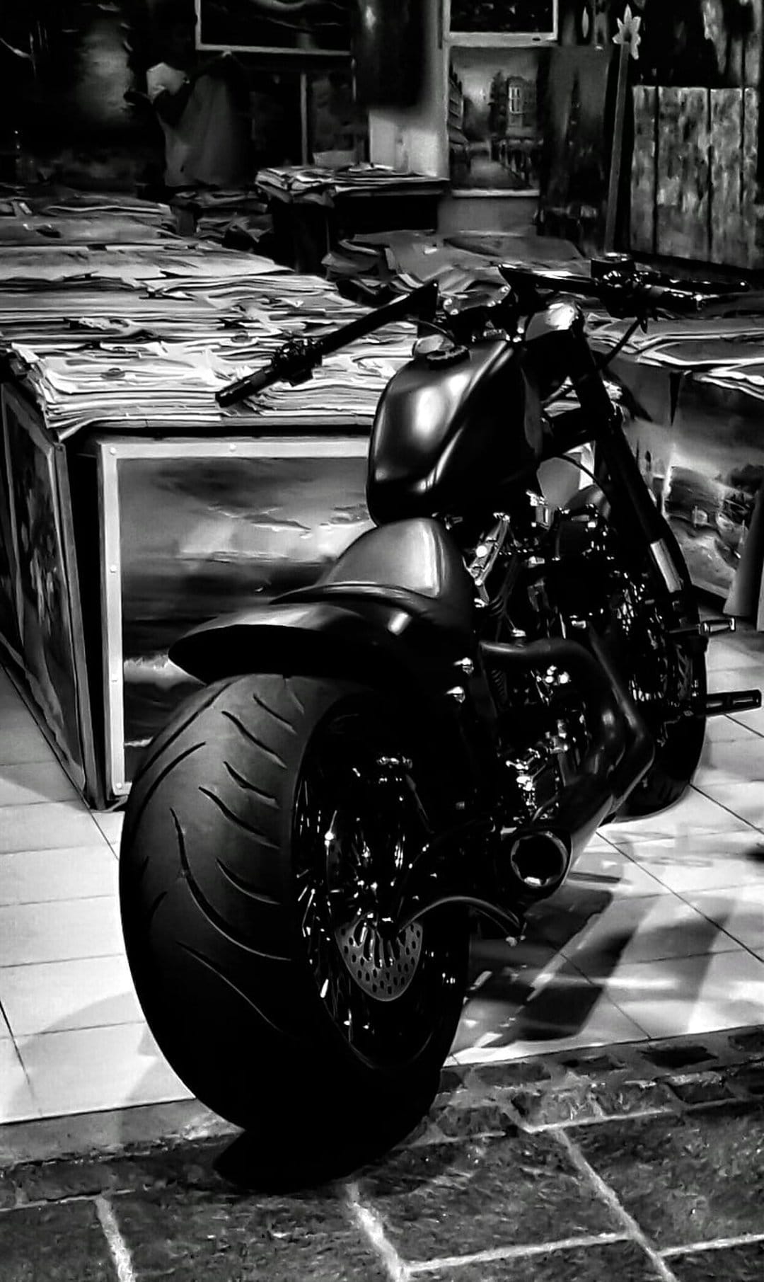 Custom chopper motorcycle with a wide rear tire parked inside a monochrome art studio filled with canvases.