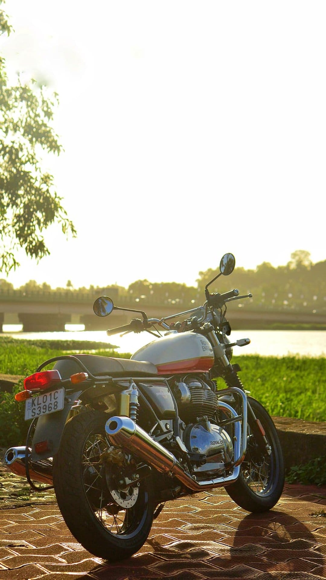 Royal Enfield Interceptor 650 with a red tank parked on a brick path near a river and bridge at sunset.