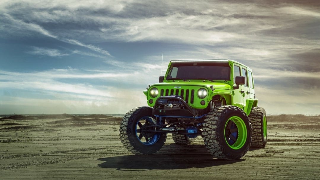 Neon green modified Jeep Wrangler with large off-road tires on a sandy beach under a dramatic cloudy sky.