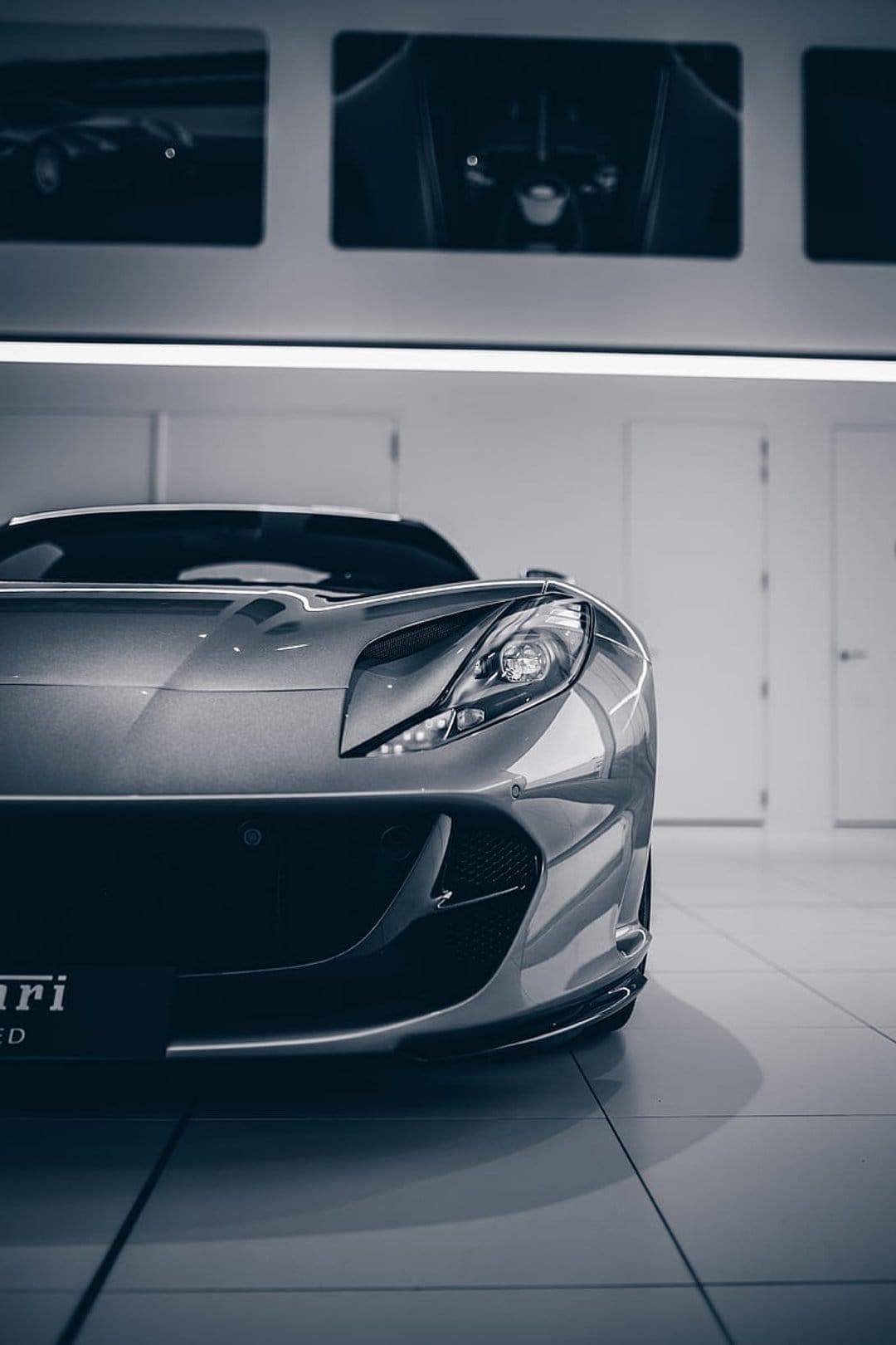 Silver Ferrari front end with aggressive headlights parked in a bright showroom with white doors and sleek floors.