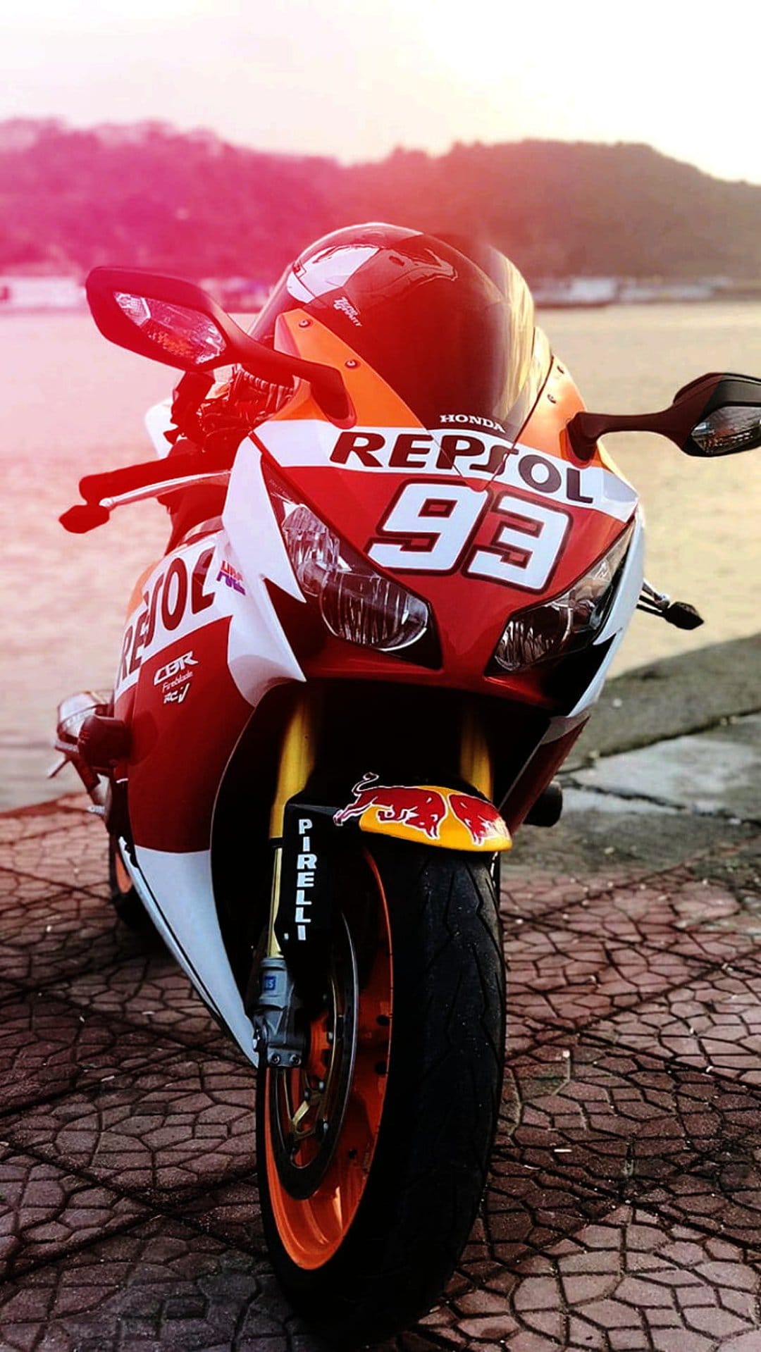 Repsol Honda CBR motorcycle with number 93 and Red Bull graphics parked on cobblestones during a sunset.