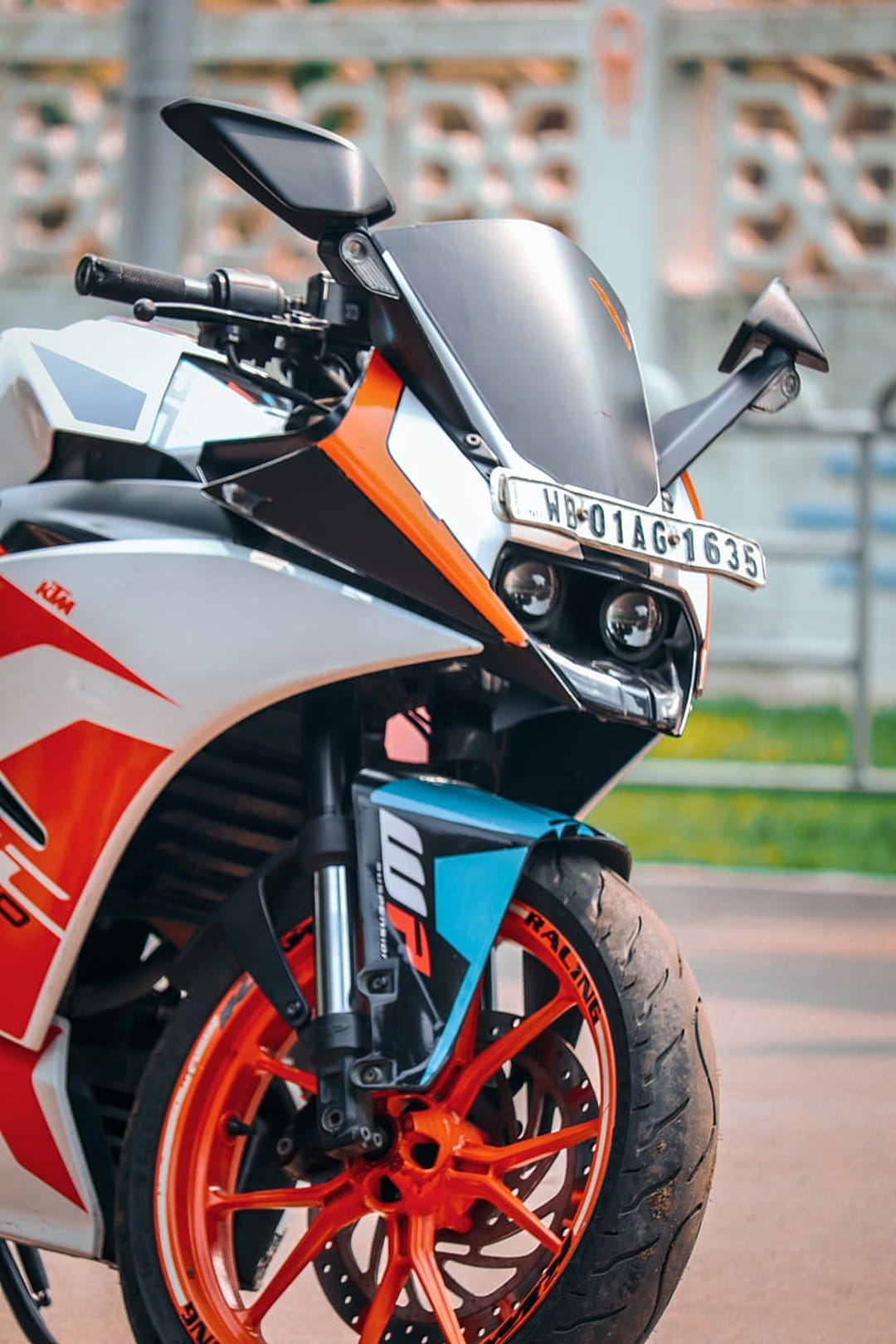 KTM RC 390 motorcycle front fairing with an orange alloy wheel, clear windshield, and sleek white body panels.