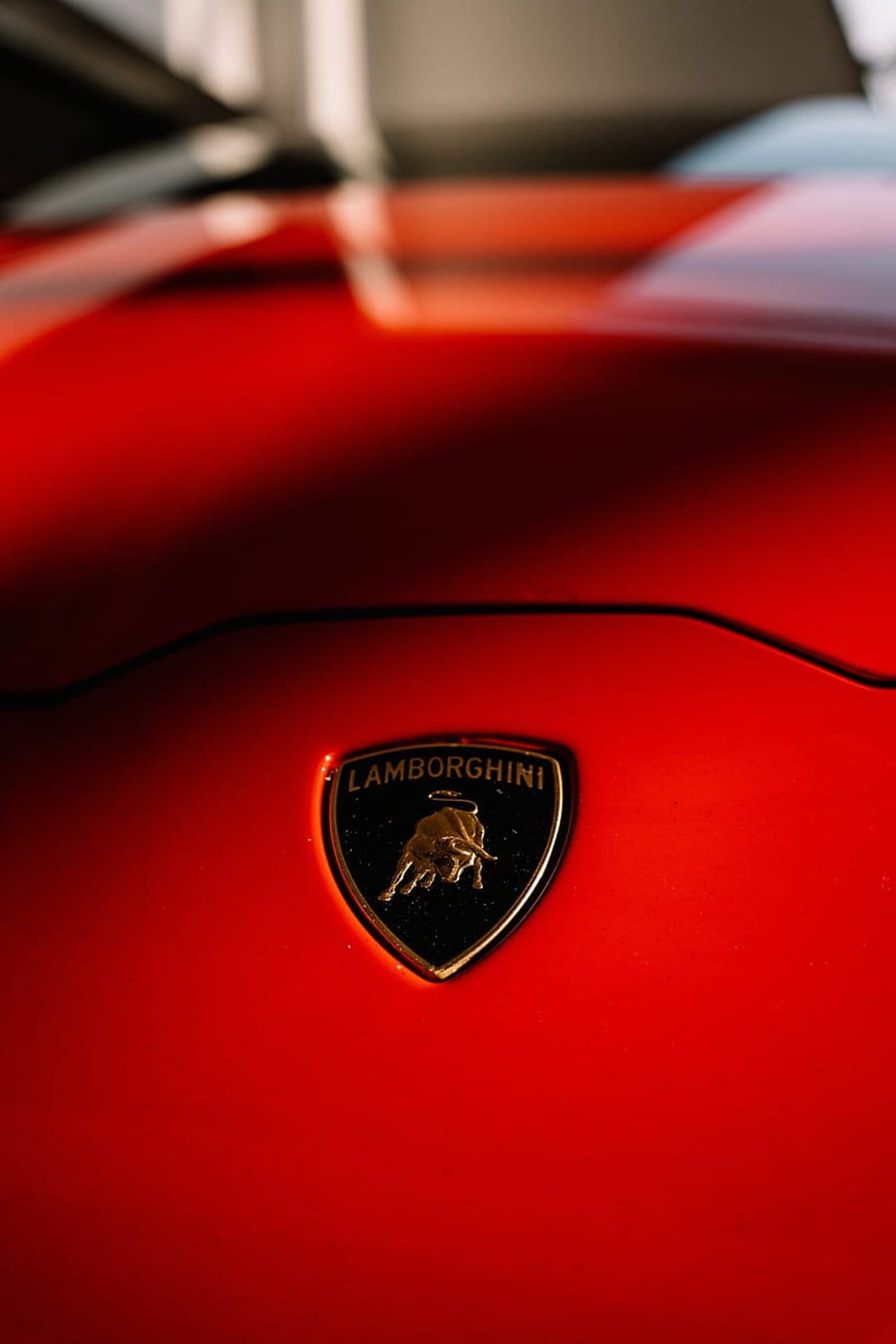 Golden Lamborghini charging bull emblem mounted on a polished red sports car hood with sleek metallic textures.