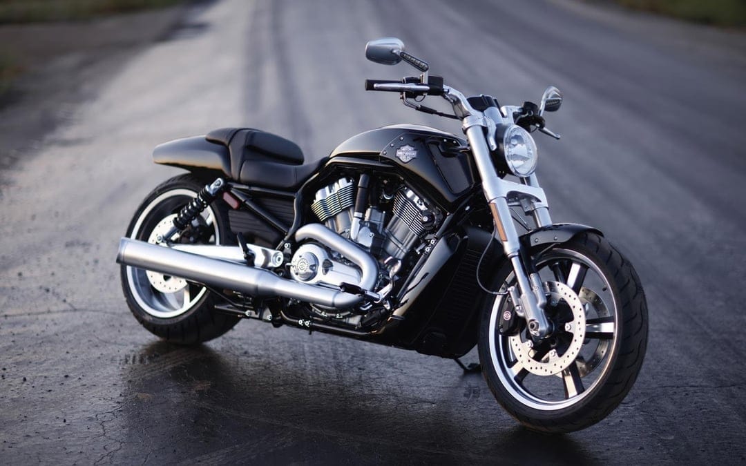 Black Harley-Davidson V-Rod motorcycle with chrome exhaust pipes parked on a blurred asphalt road in soft light.